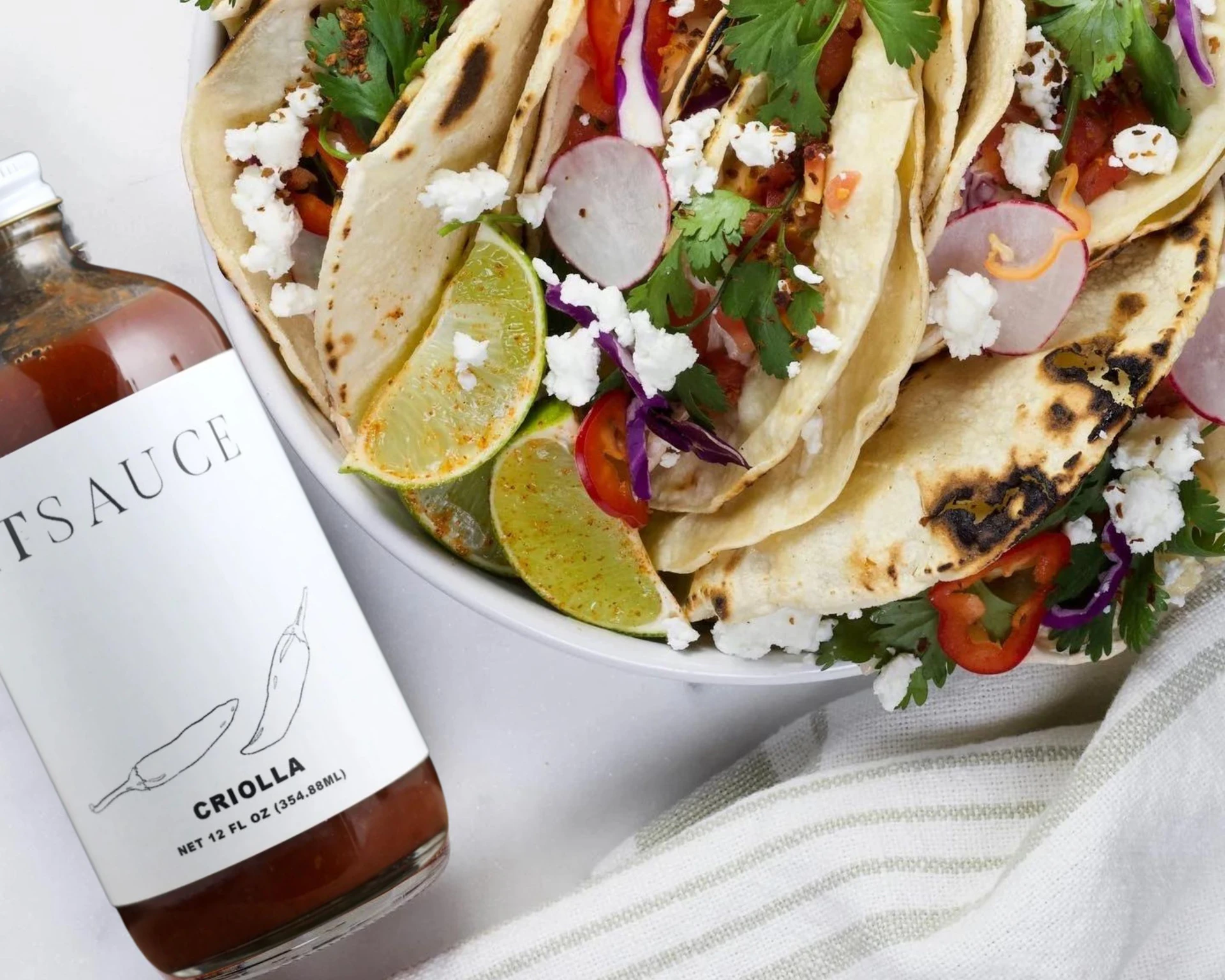 a plate of tacos next to a bottle of sauce