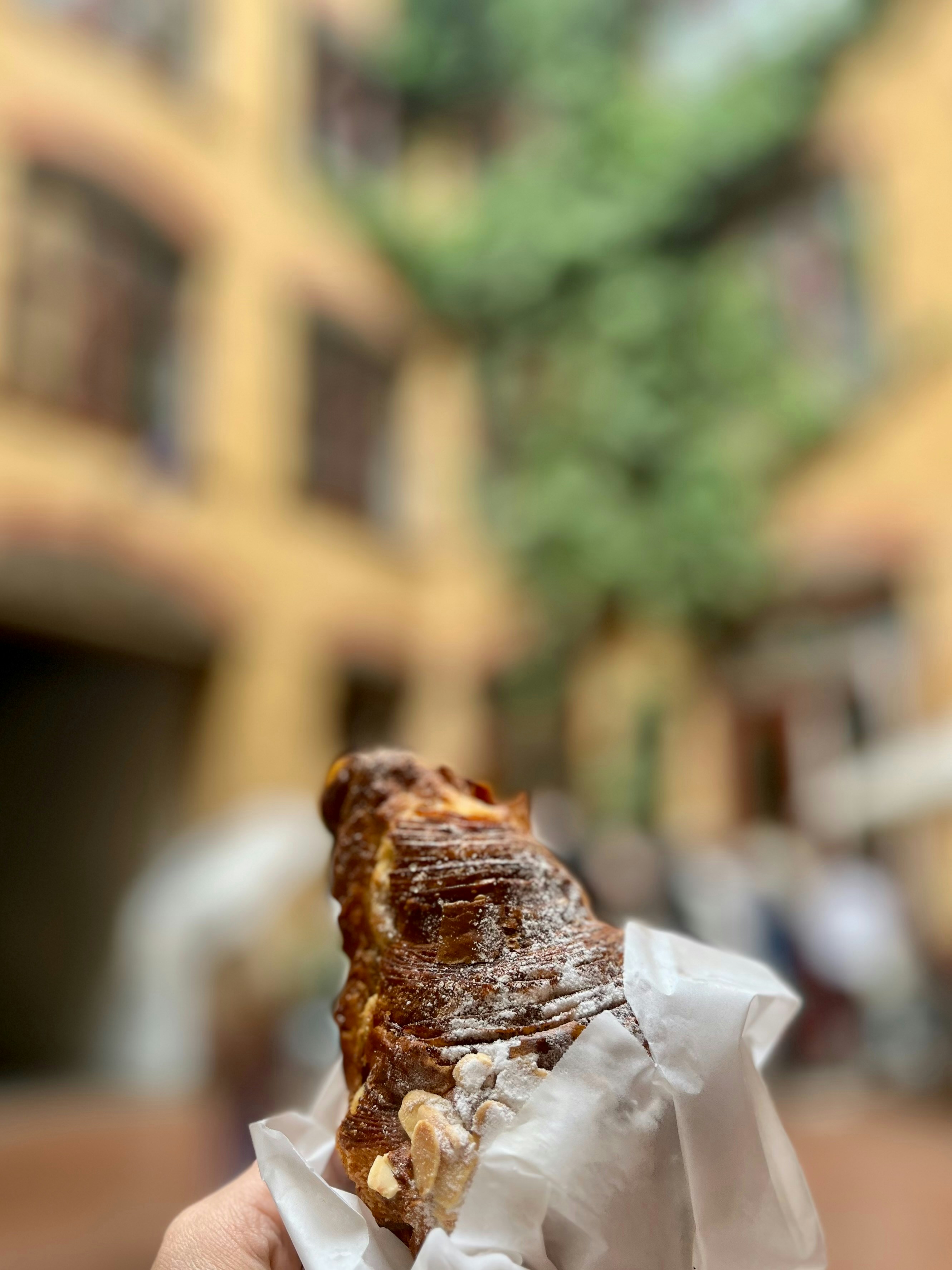 Golden flaky almond croissant dusted with powdered sugar on parchment paper in warm light