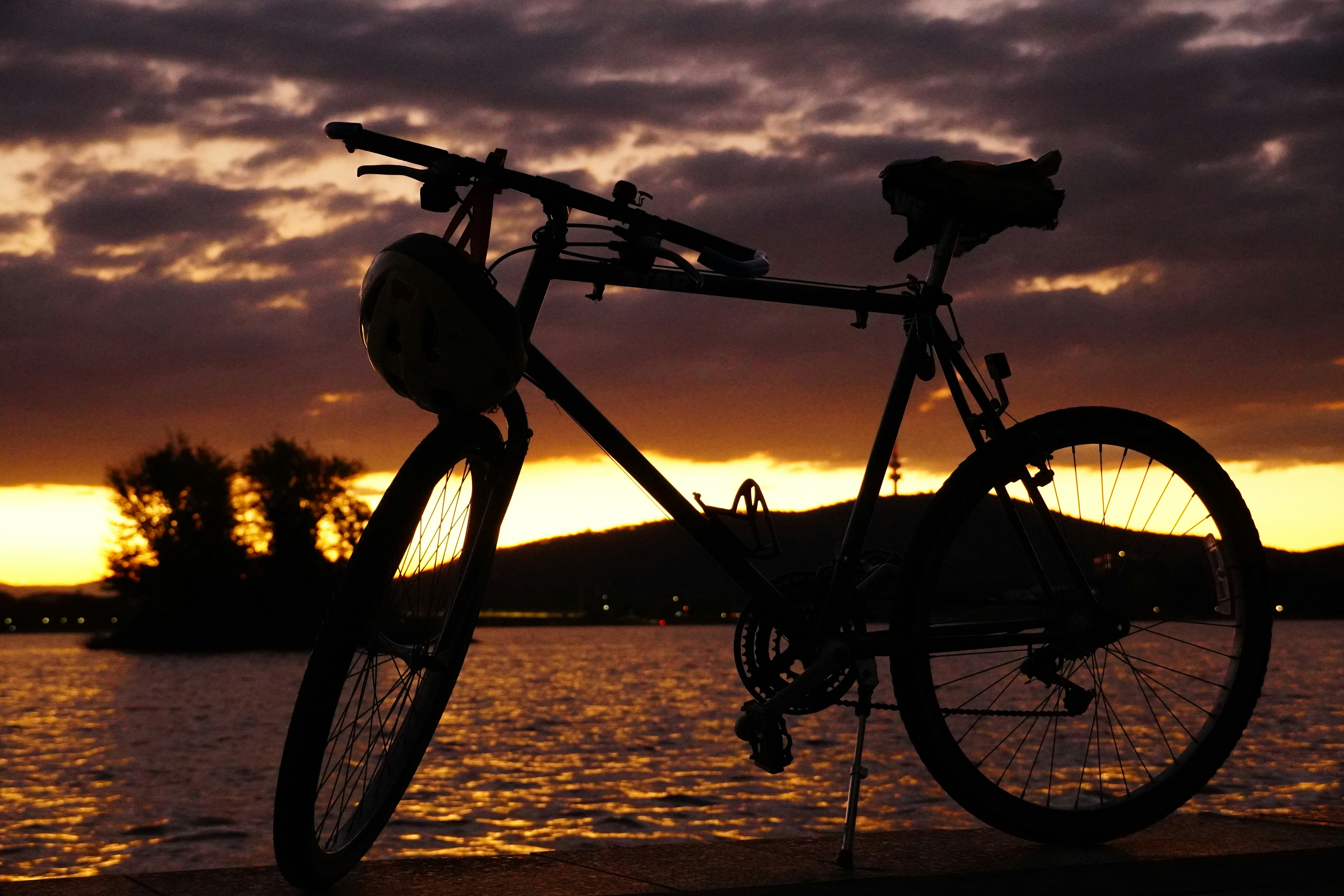 a bike parked on the side of a lake at sunset