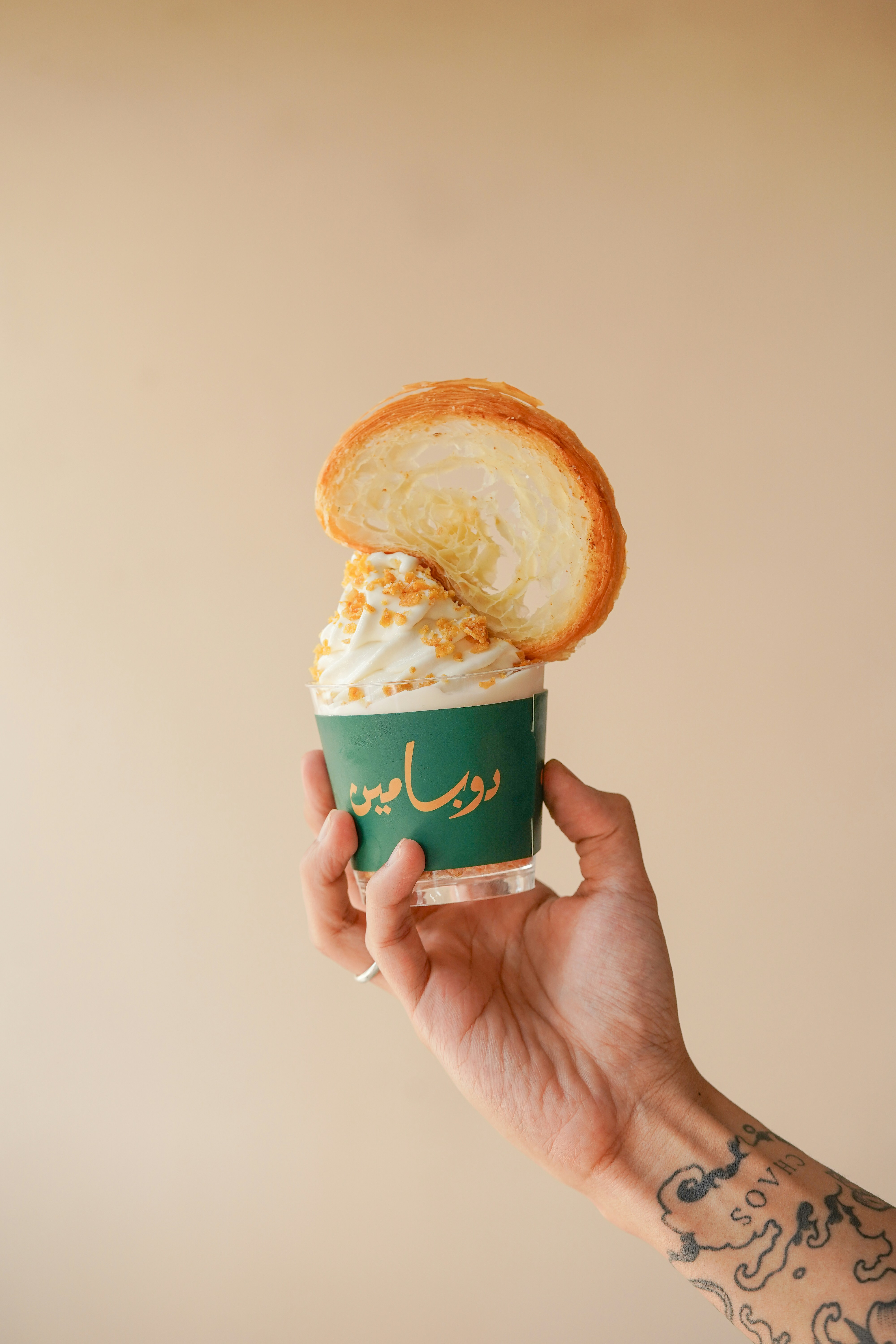 a hand holding a cup of ice cream with a pastry on top of it