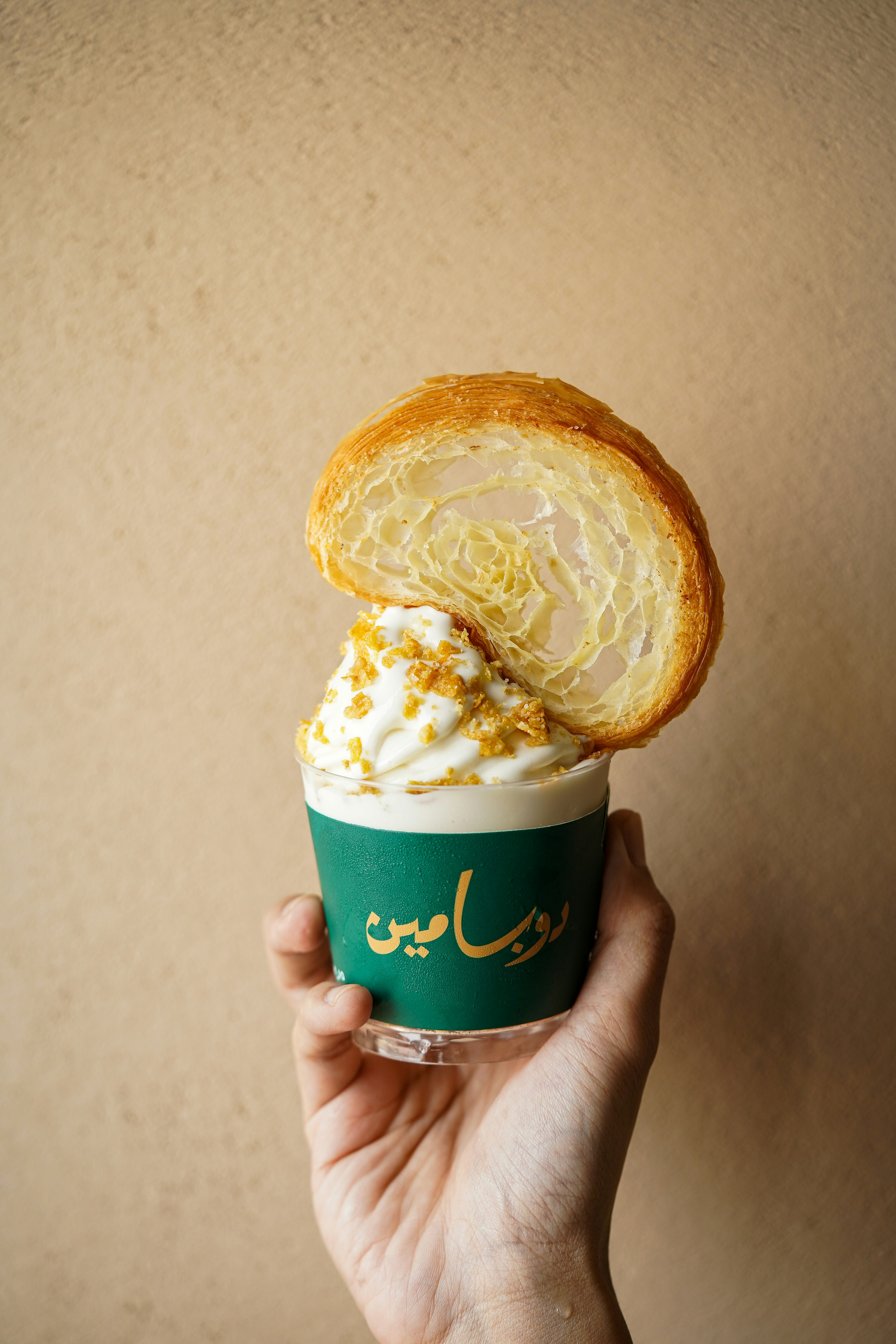 a person holding a cup with a pastry on top of it