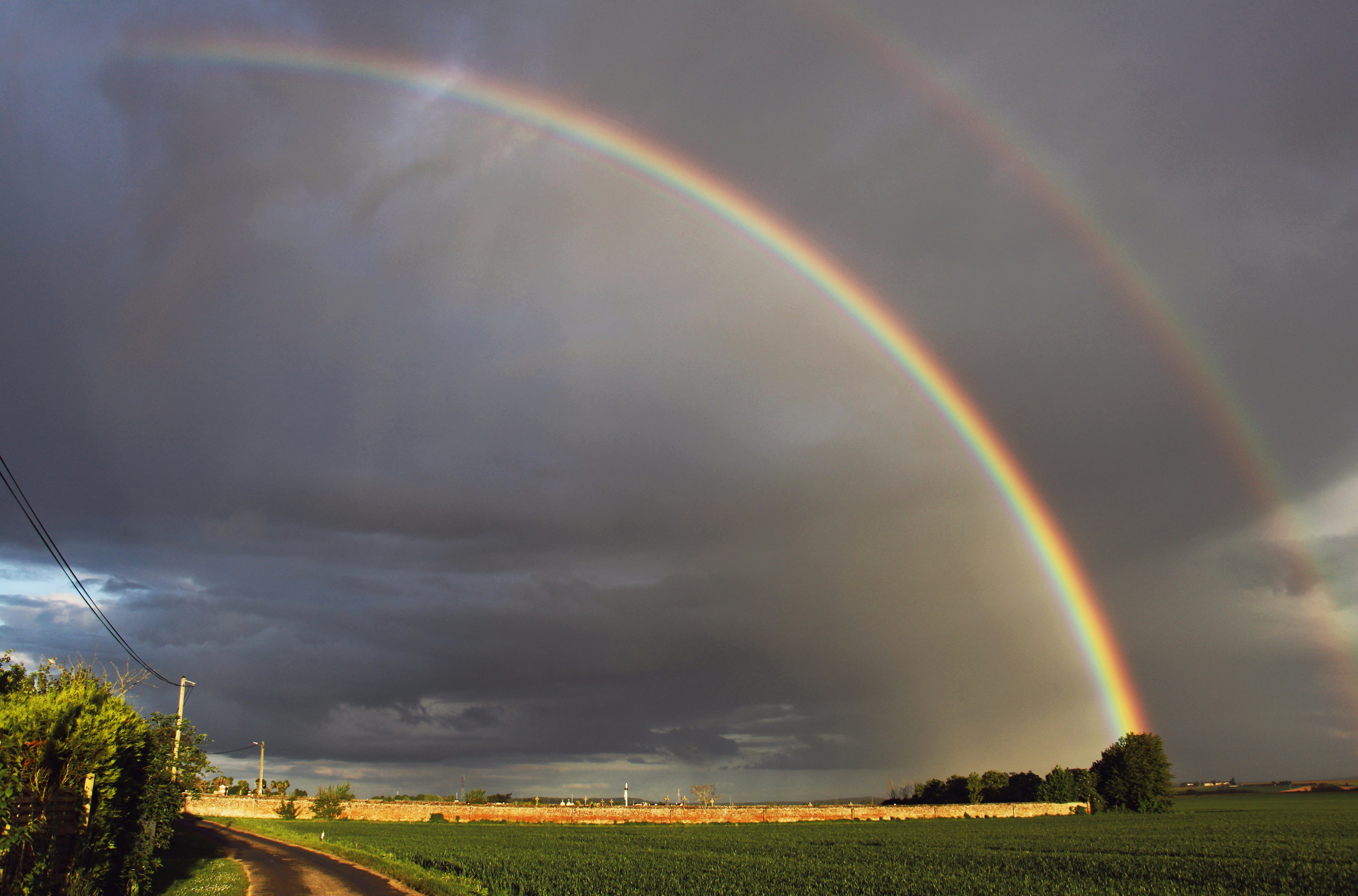 Due arcobaleni in un cielo nuvoloso su una strada sterrata