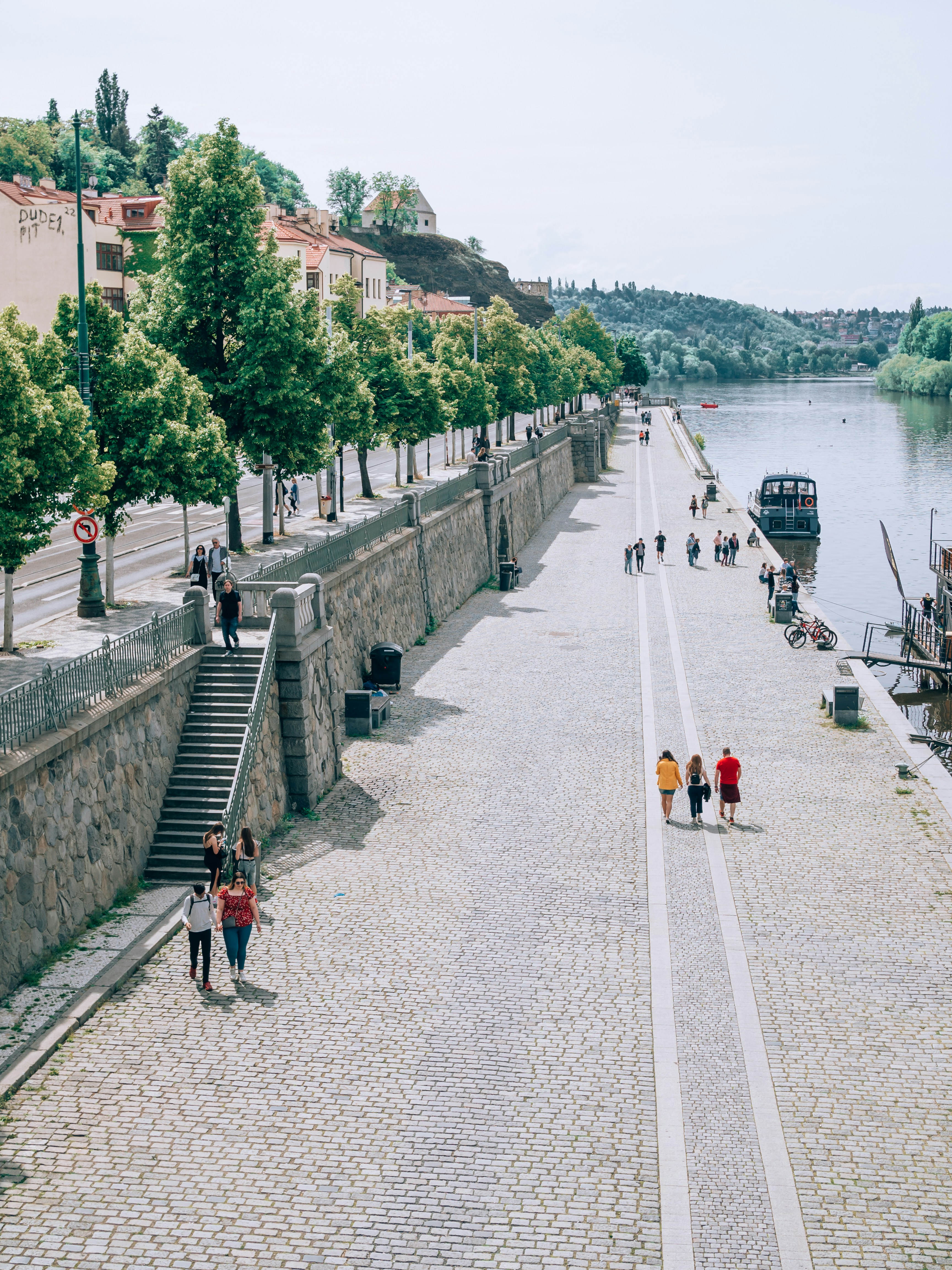 a group of people walking down a cobblestone road next to a river