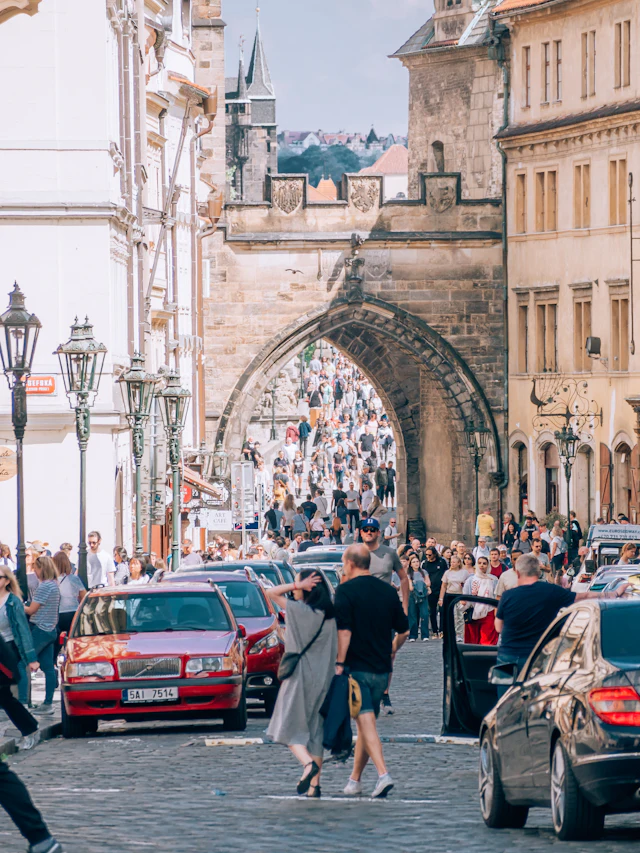 Crowds passing through the gothic archway of the Malá Strana Bridge Tower at the Charles Bridge entrance.