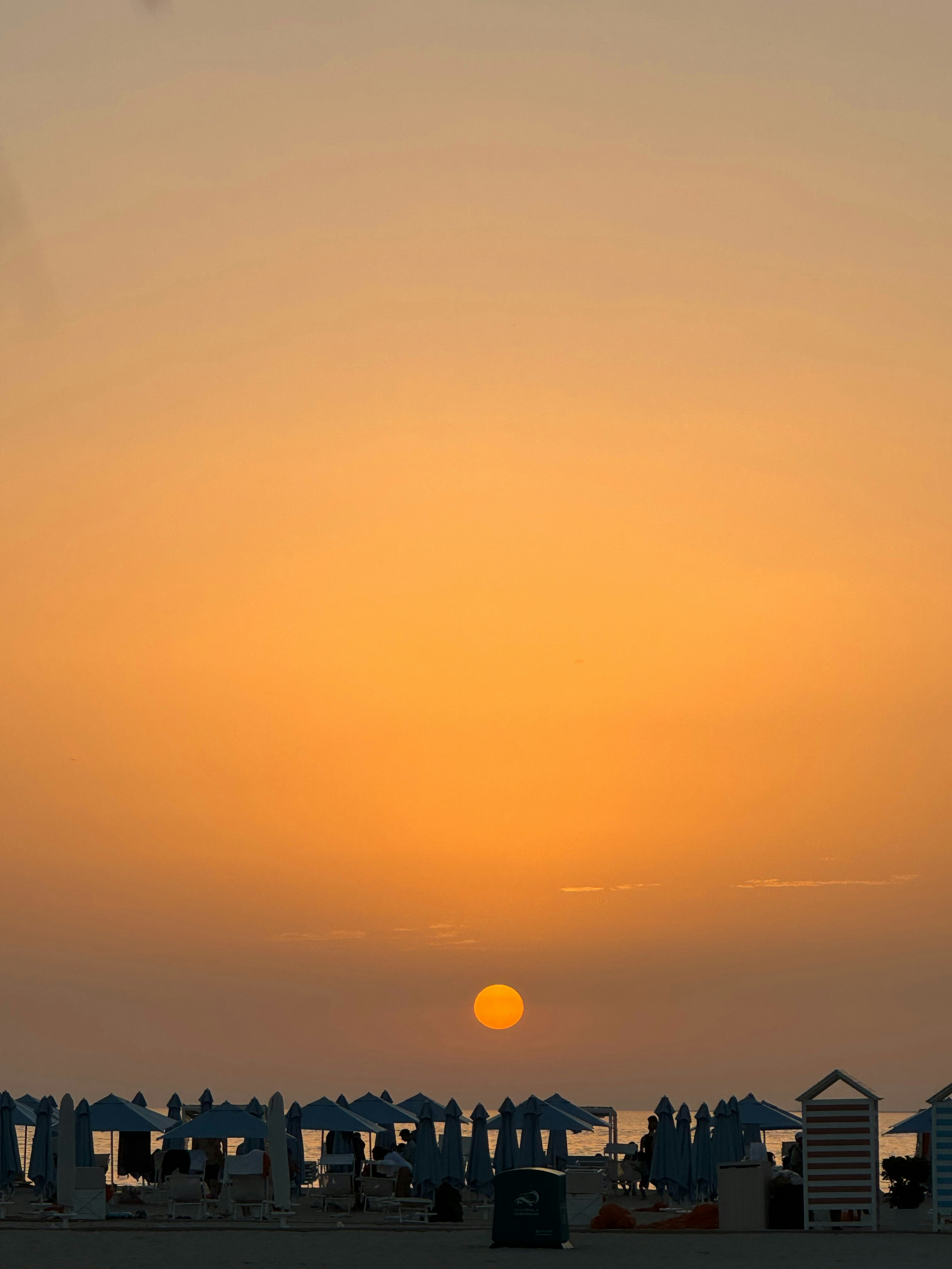 the sun is setting over a beach with umbrellas