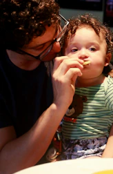 a man feeding a small child a piece of food