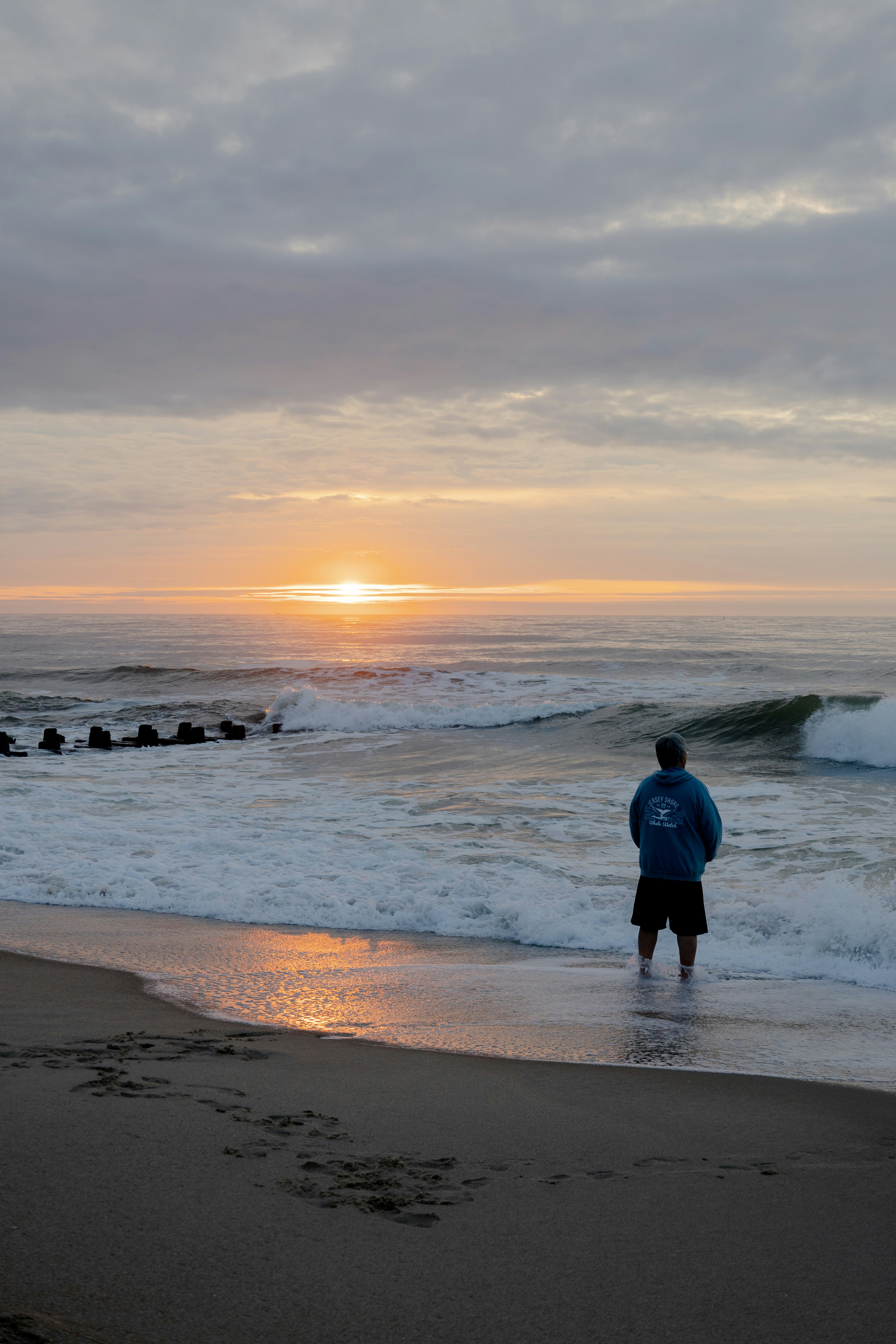 A man standing on top of a beach next to the ocean photo Free Nj