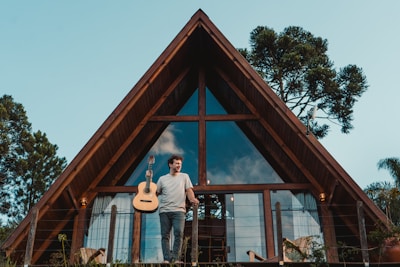 a man holding a guitar standing in front of a house