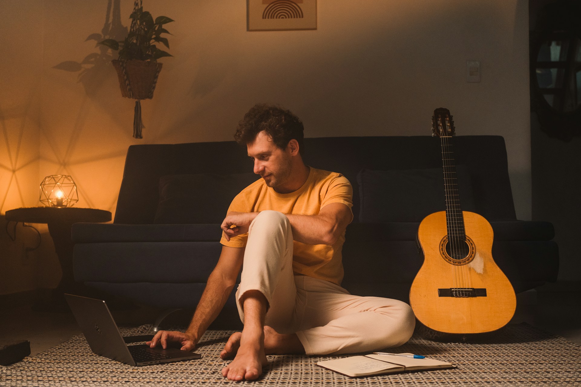 a man sitting on the floor with a laptop and a guitar