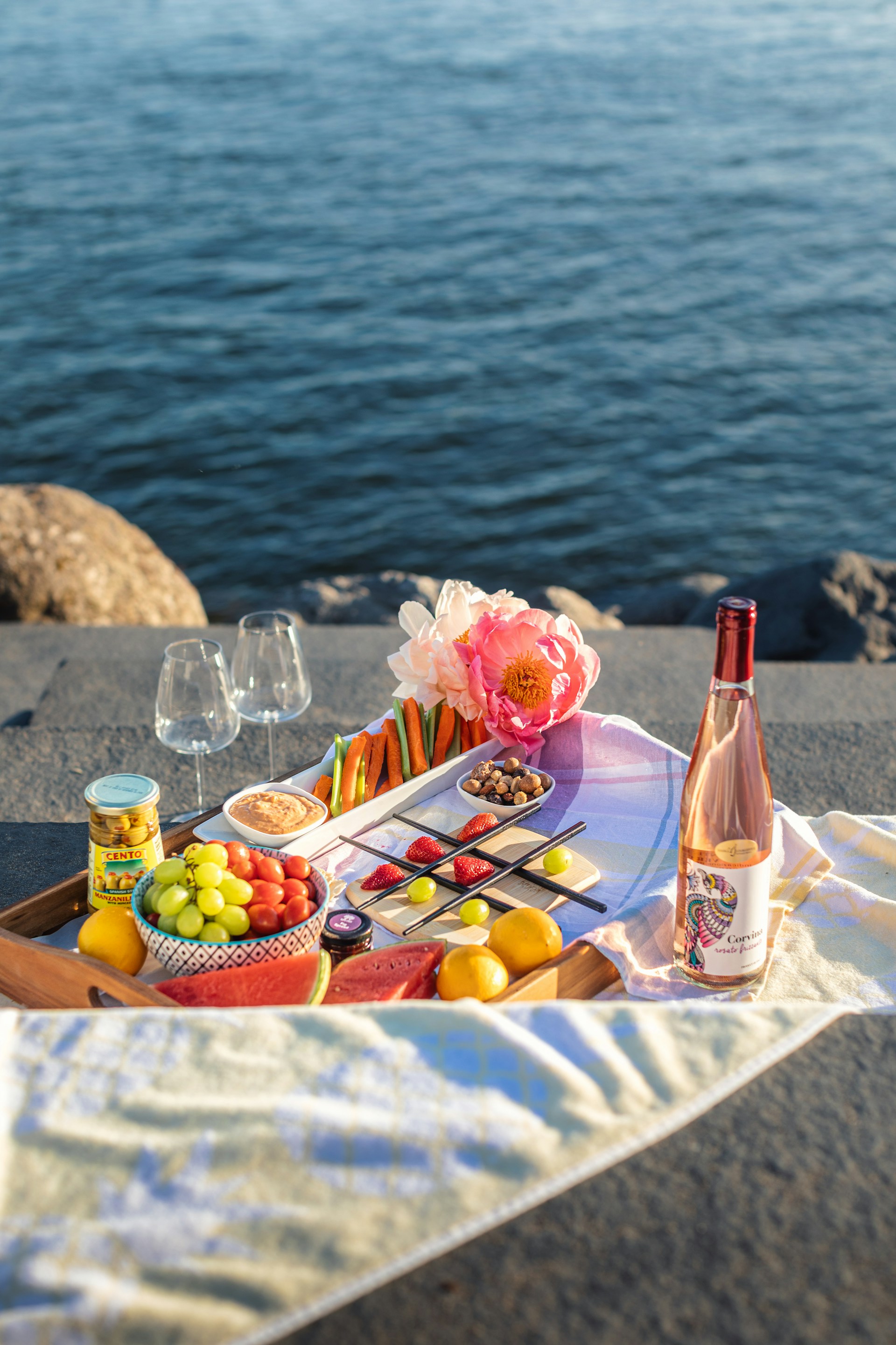 a tray of food and a bottle of wine on a beach