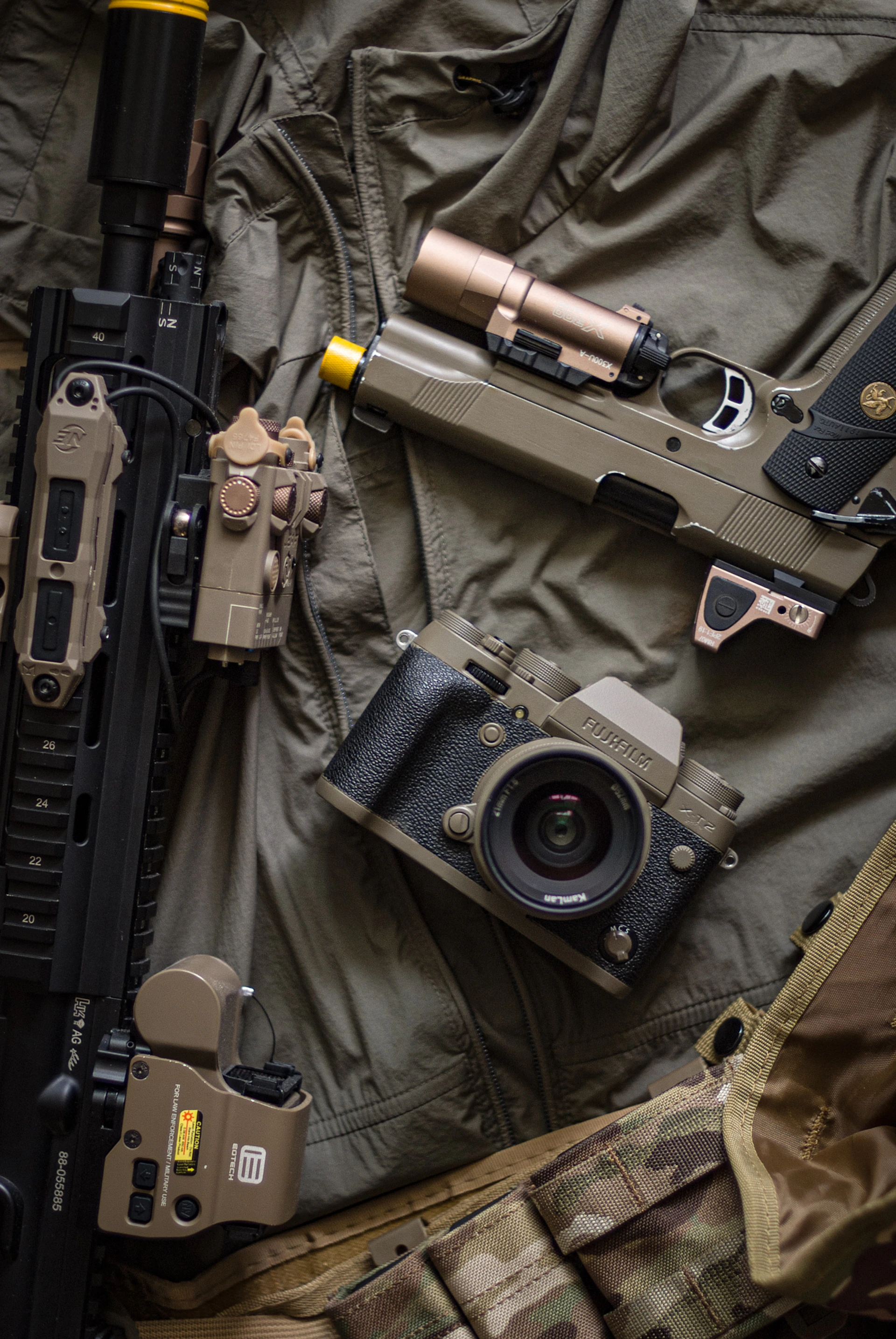 a rifle, a camera, and other items laid out on a blanket