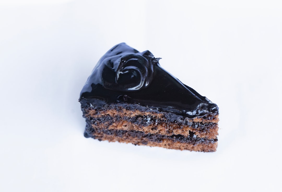 a piece of chocolate cake on a white surface, Chocolate Truffle Pastry: Decadent and delightful, a bite-sized explosion of rich chocolate.