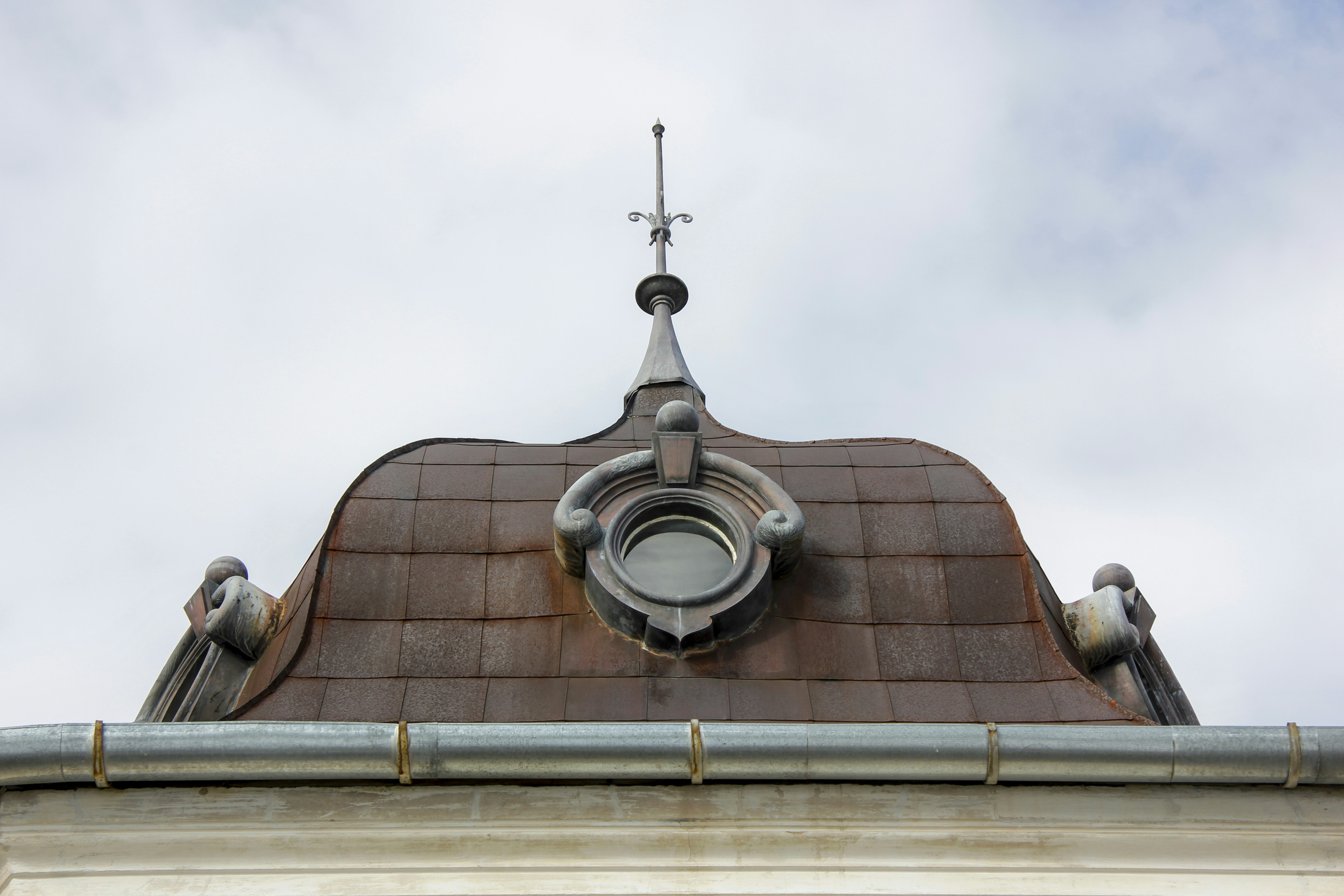 Ornate metal roof with a circular dormer and pointed finial.