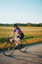 A woman in a helmet and purple jersey cycling along a country road