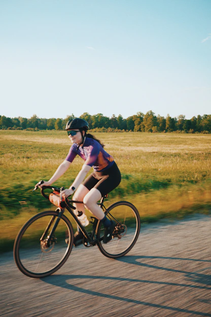 A woman in a helmet and purple jersey cycling along a country road