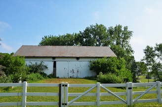 a white barn sits behind a white fence