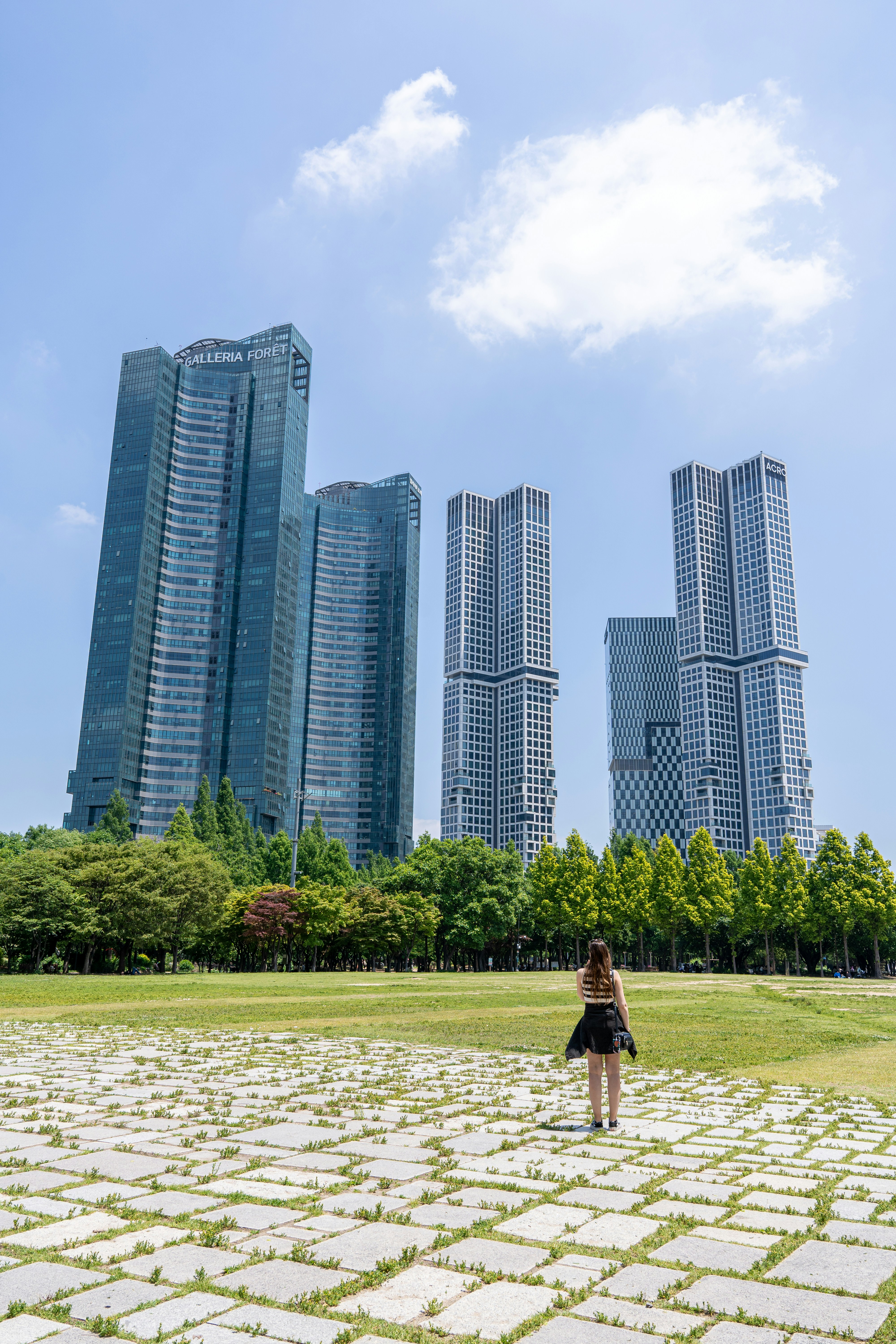 une femme debout dans un champ devant de grands immeubles