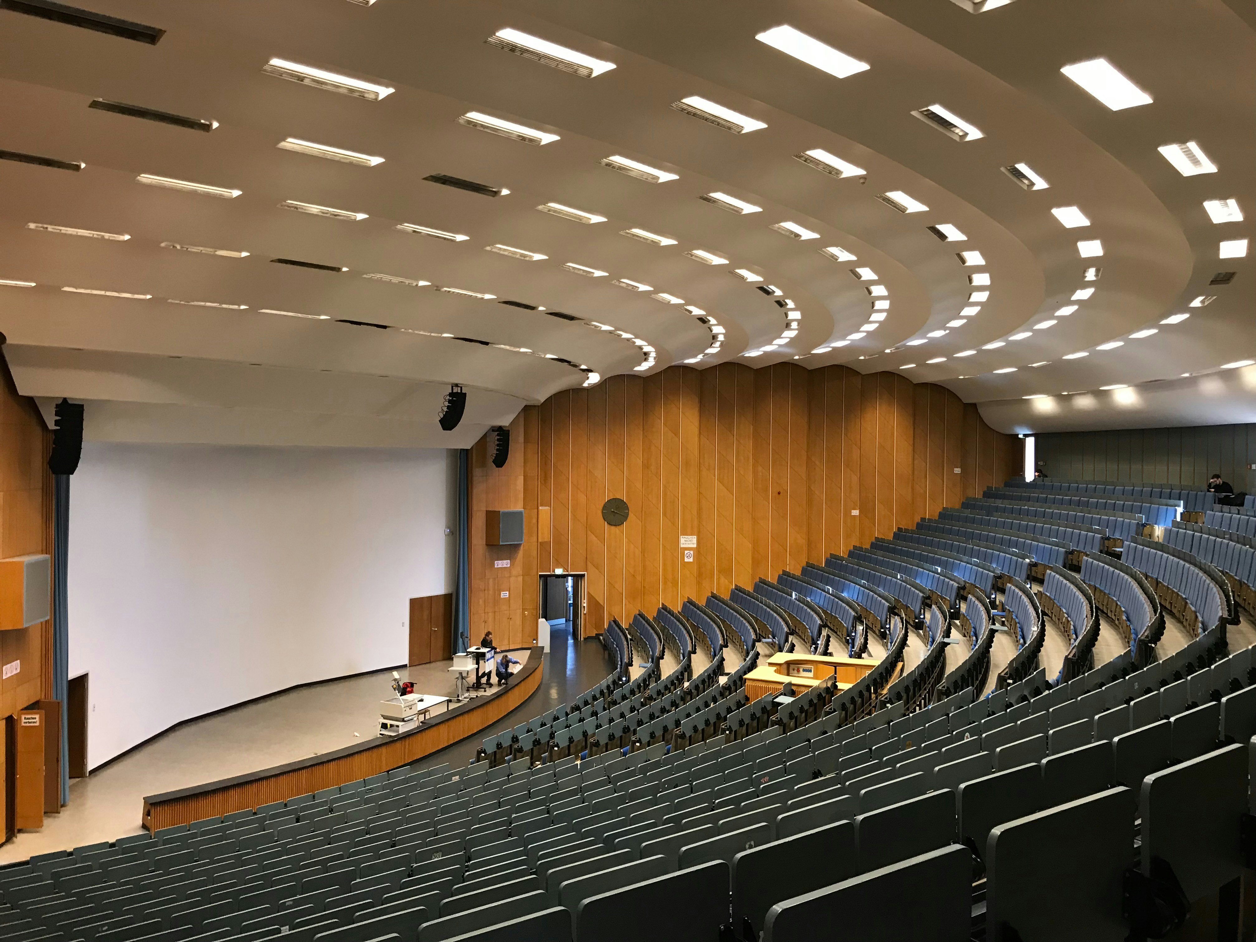 Lecture hall with dim ambient lighting, dark ceiling with scattered warm spotlights on empty seats