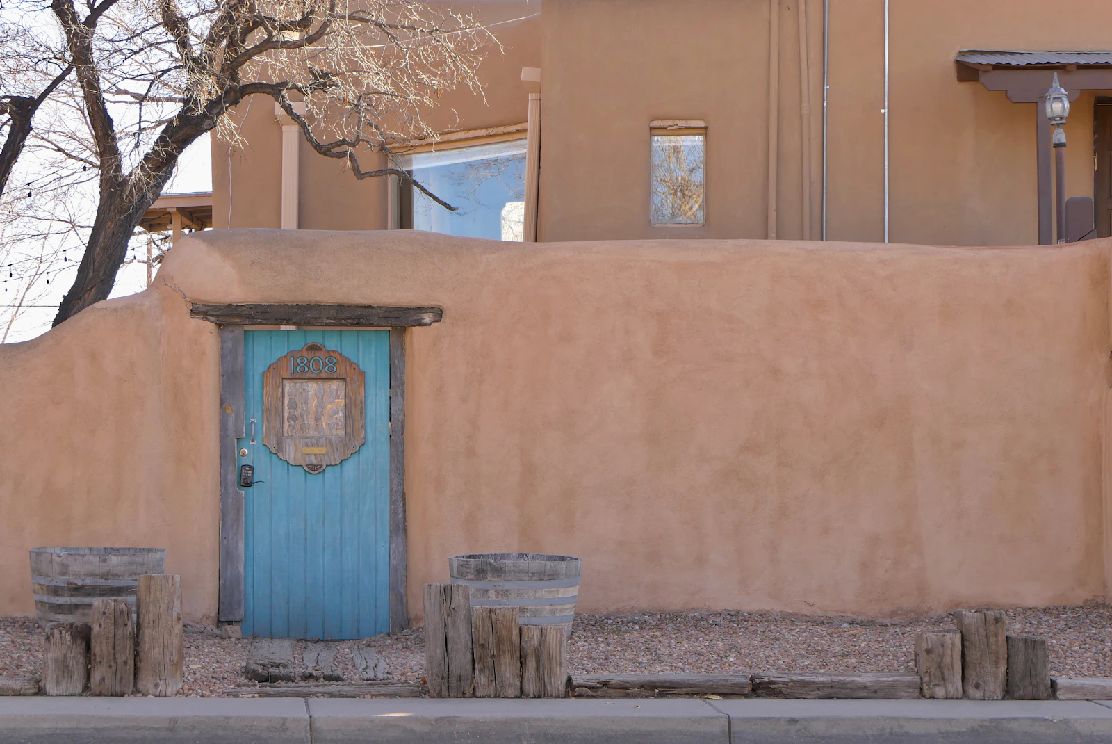 A Santa Fe adobe wall with a turquoise wooden door under a clear sky
