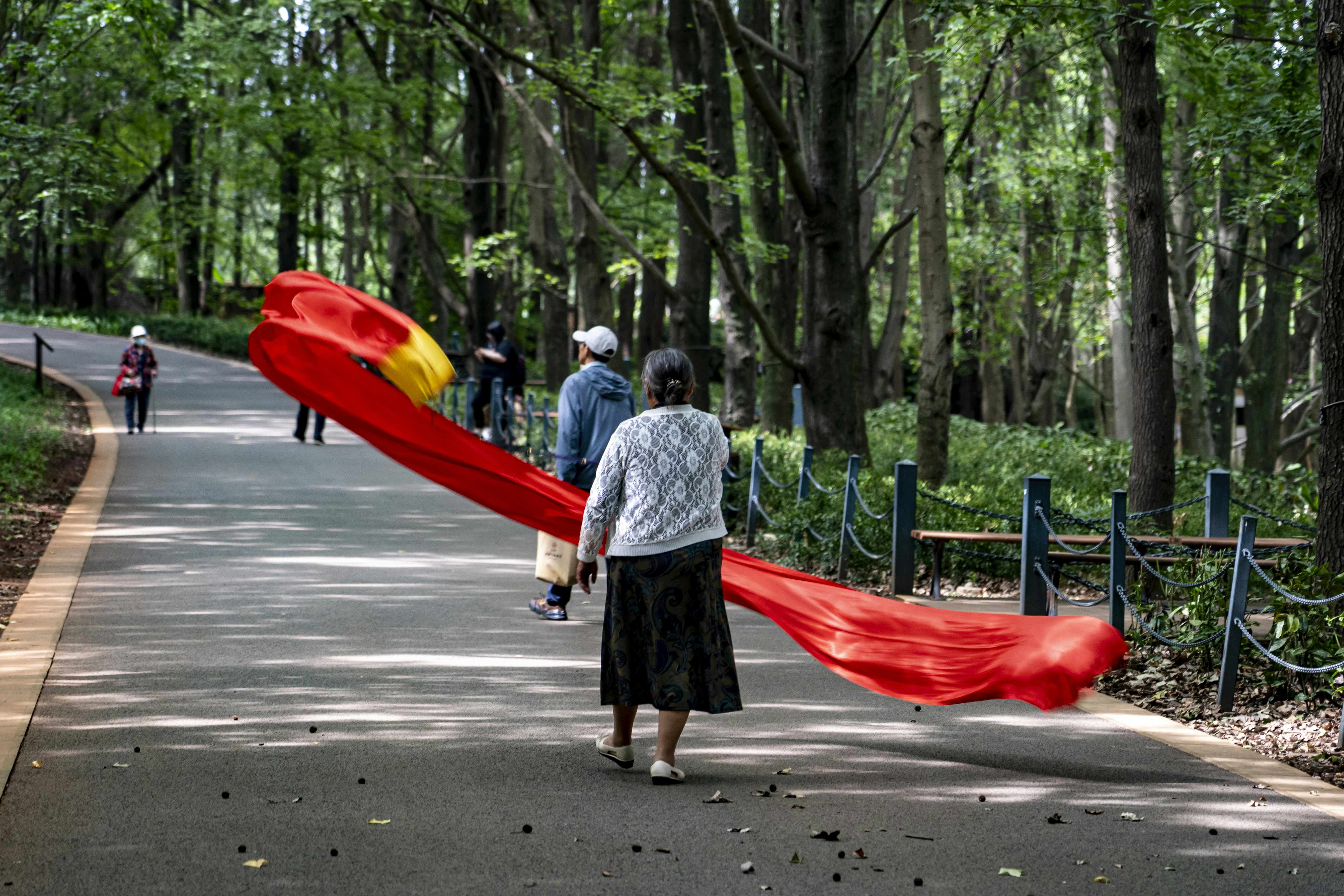 a woman walking down a road holding a red scarf