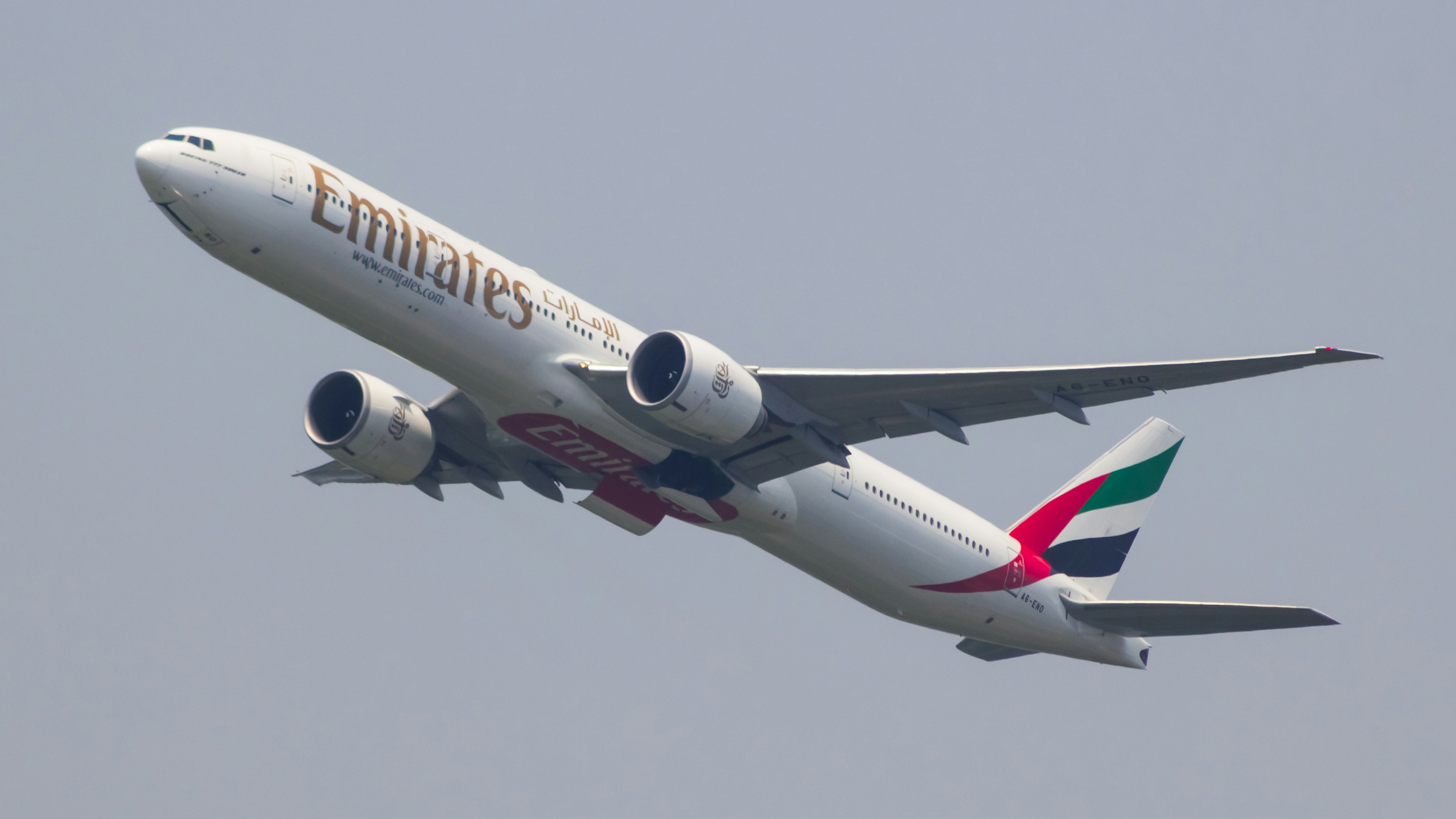 a large passenger jet flying through a gray sky, Emirates Boeing 777-300ER retracting it