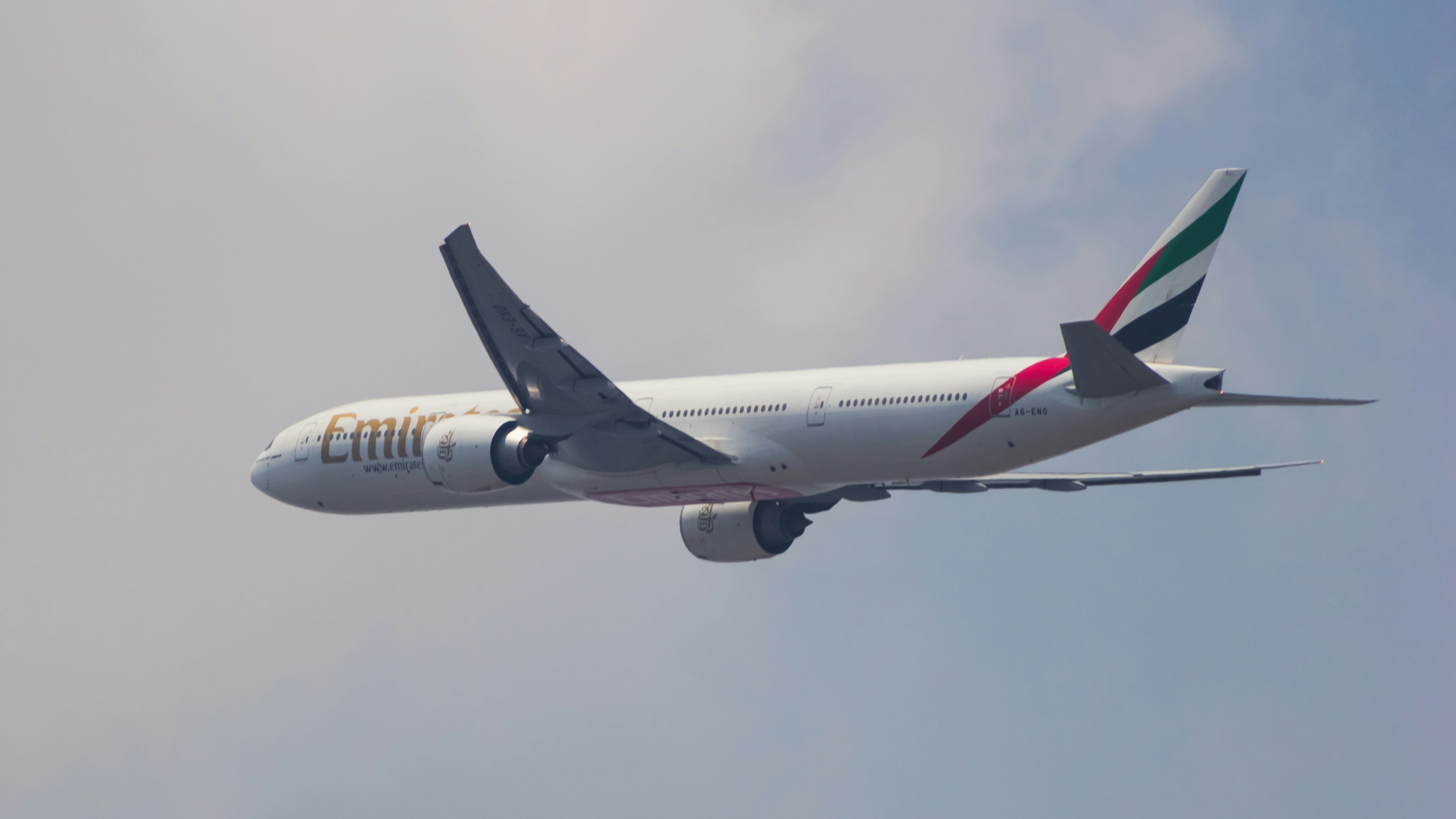 a large jetliner flying through a cloudy blue sky, Emirates Boeing 777-300ER
