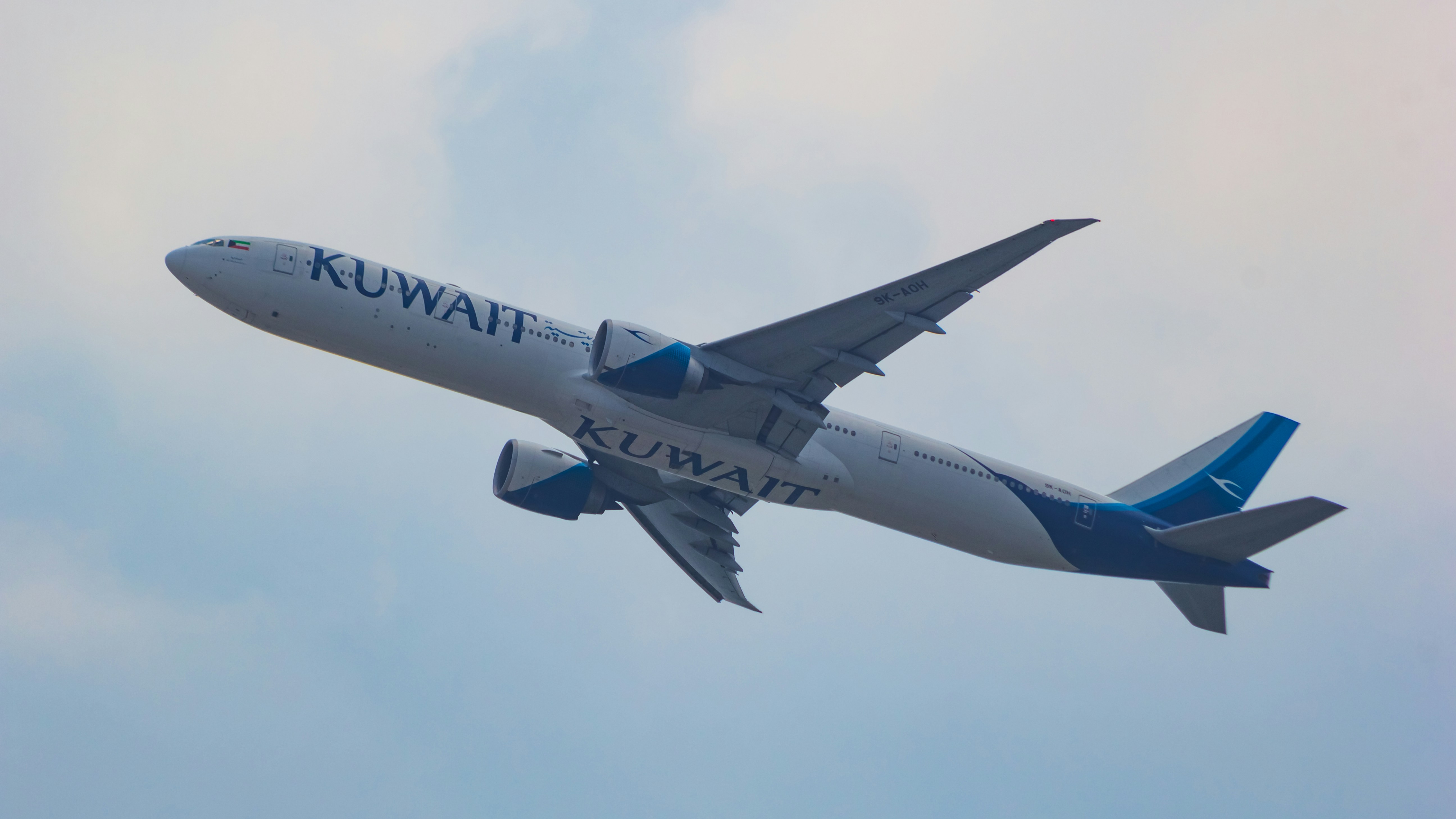 a large jetliner flying through a cloudy blue sky, Kuwait Airways Boeing 777-300ER