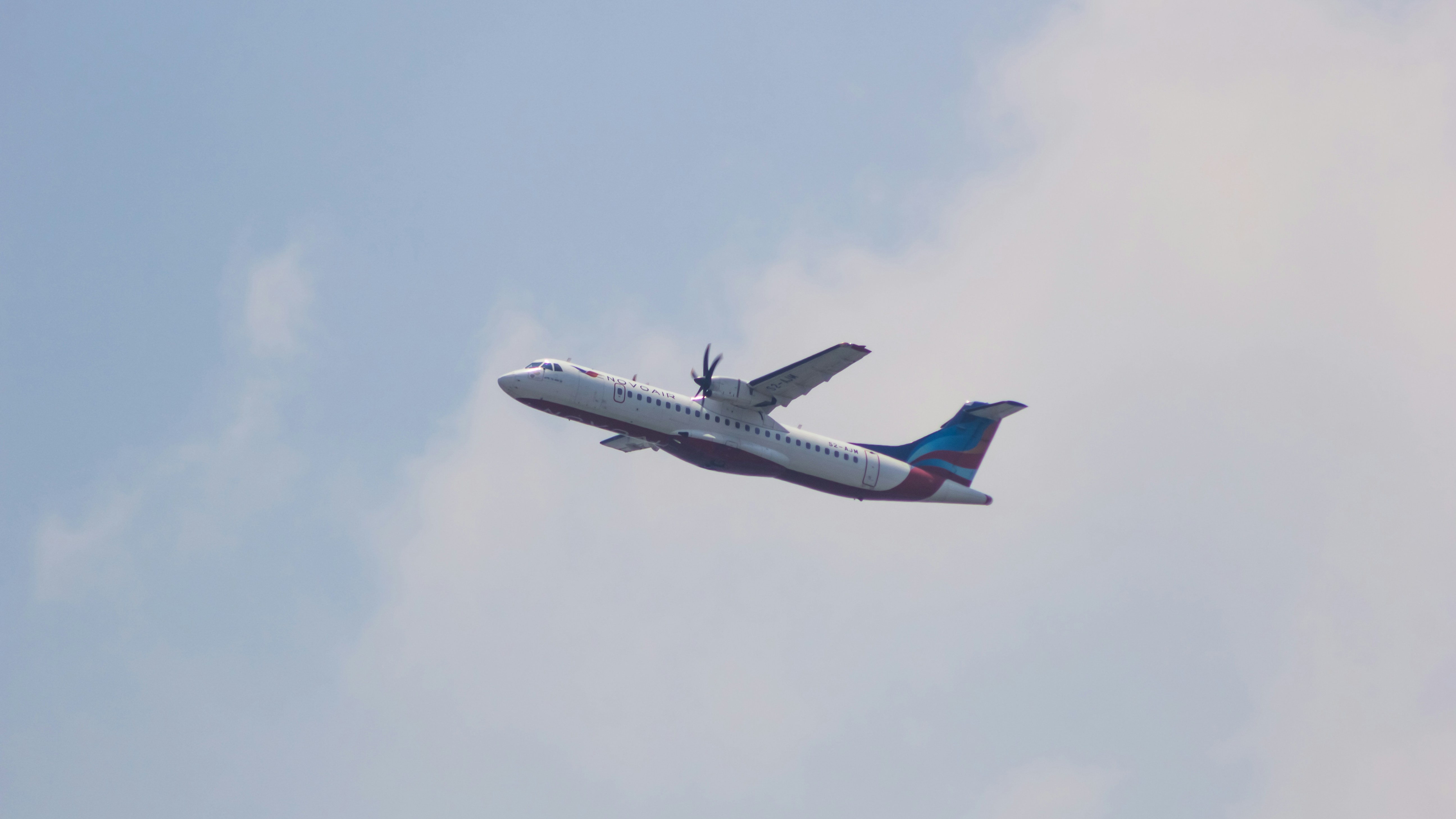 a large passenger jet flying through a cloudy blue sky, Novoair ATR 72-600 flying