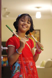 a girl in a red dress holding a pair of sticks