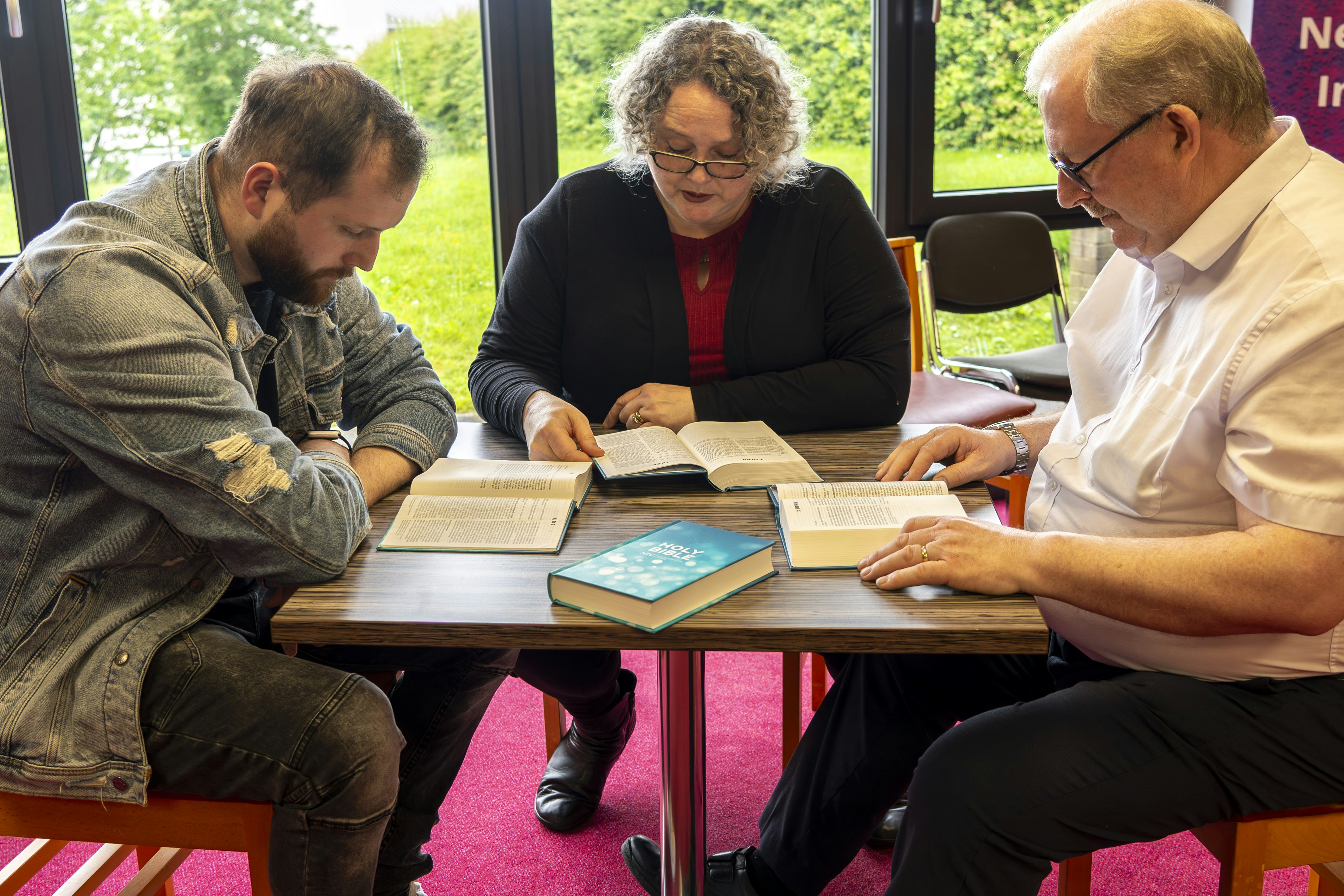 three people sitting at a table with open books