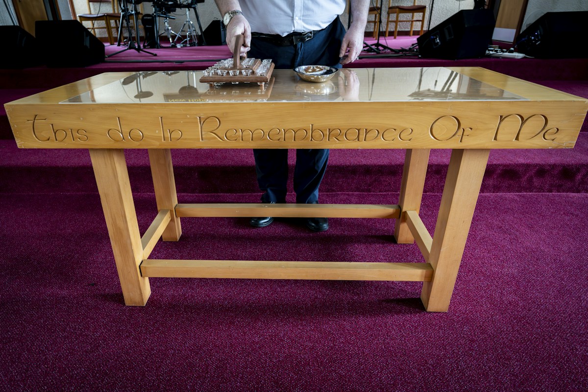 A man stands by a table with church volunteer sign-up sheets and pens, ready for congregation members to register.