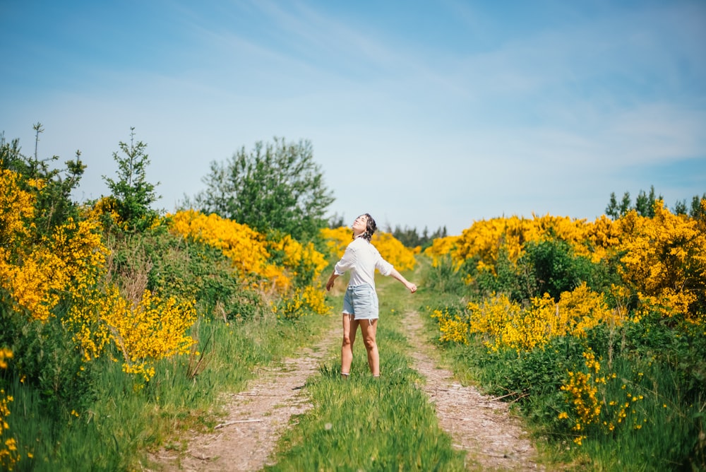 a woman standing on a dirt road surrounded by yellow flowers