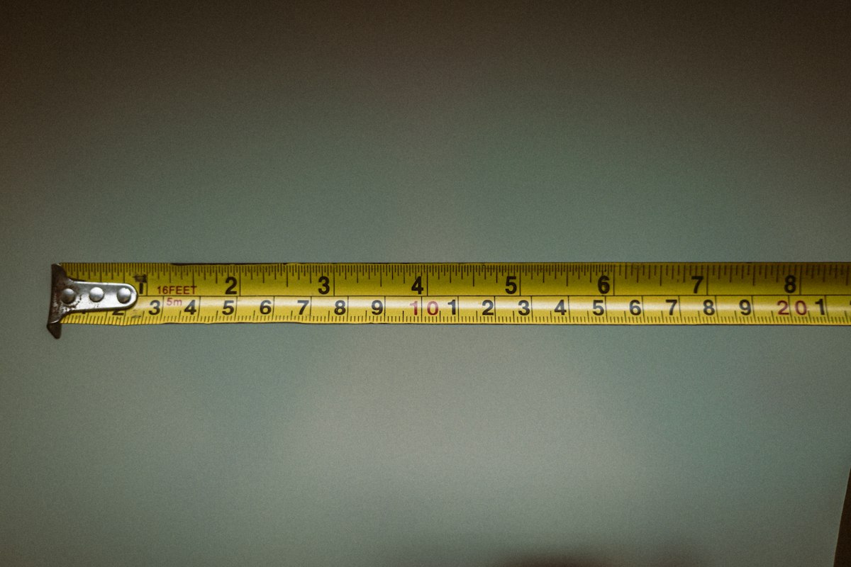 Yellow tape measure extended across a plain wall, showing imperial and metric measurements.