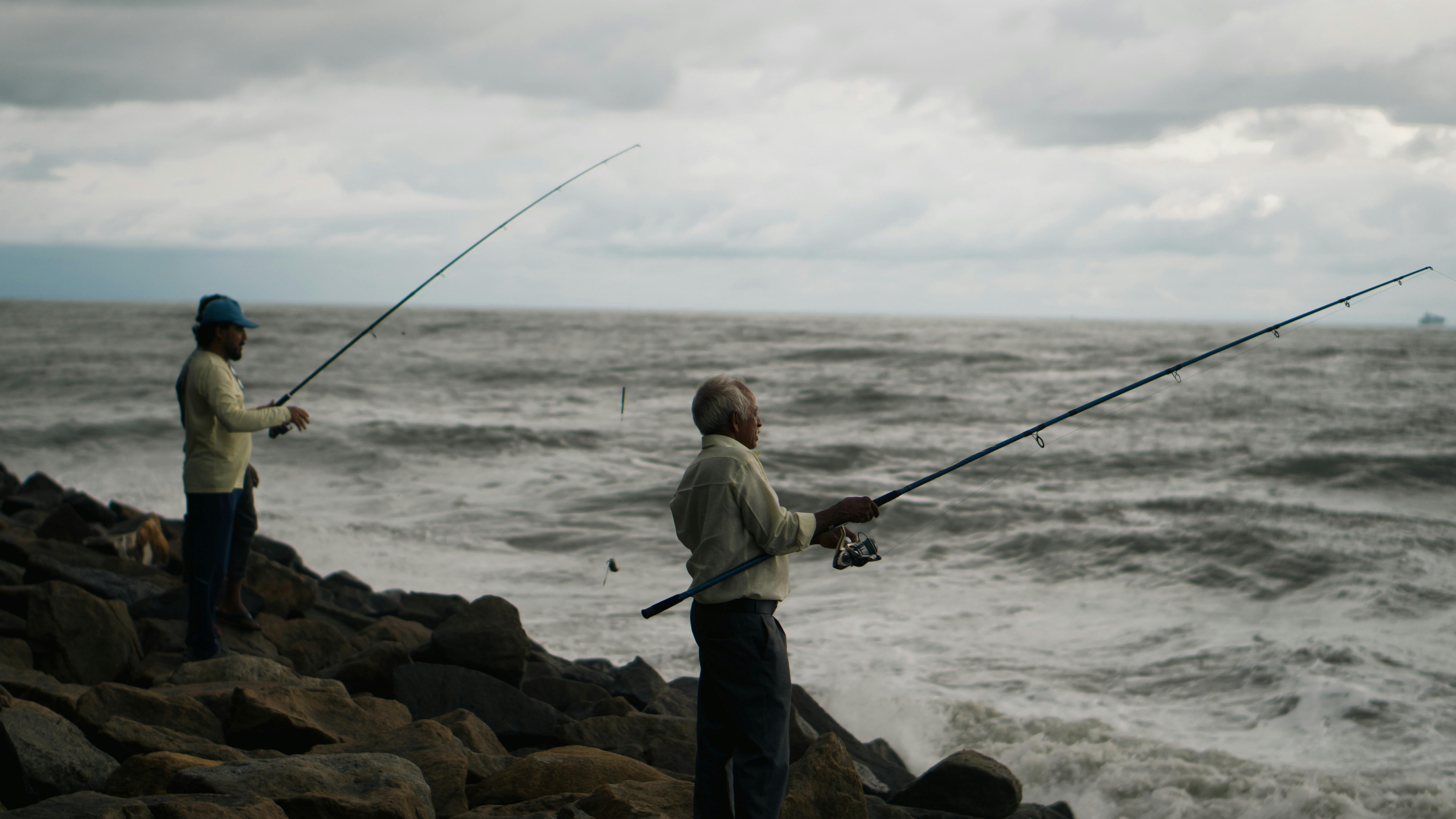 A couple of men standing on top of a rocky beach photo – Free Grey ...