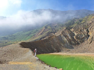 a man standing on the edge of a cliff next to a green lake
