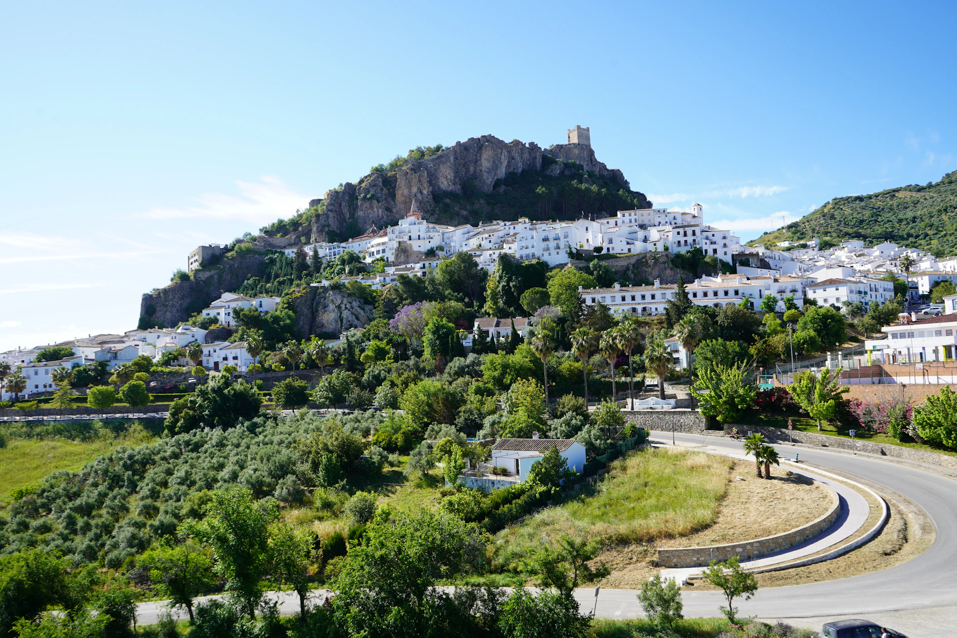 a car driving down a road next to a lush green hillside
