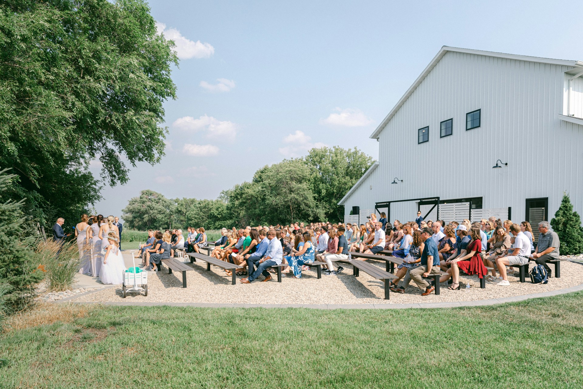 a group of people sitting on benches in front of a barn