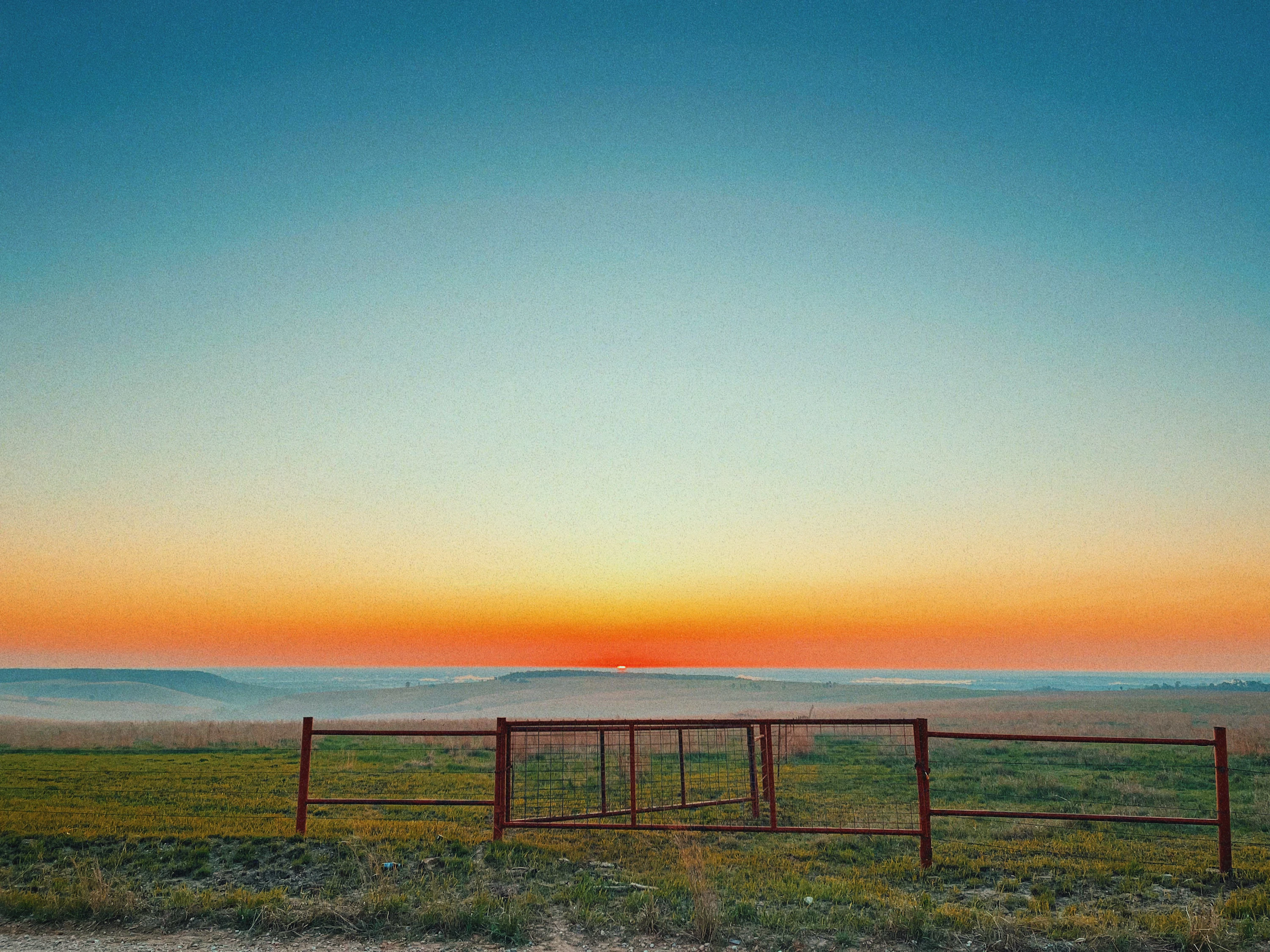 A red gate in an Oklahoma prairie field at sunset