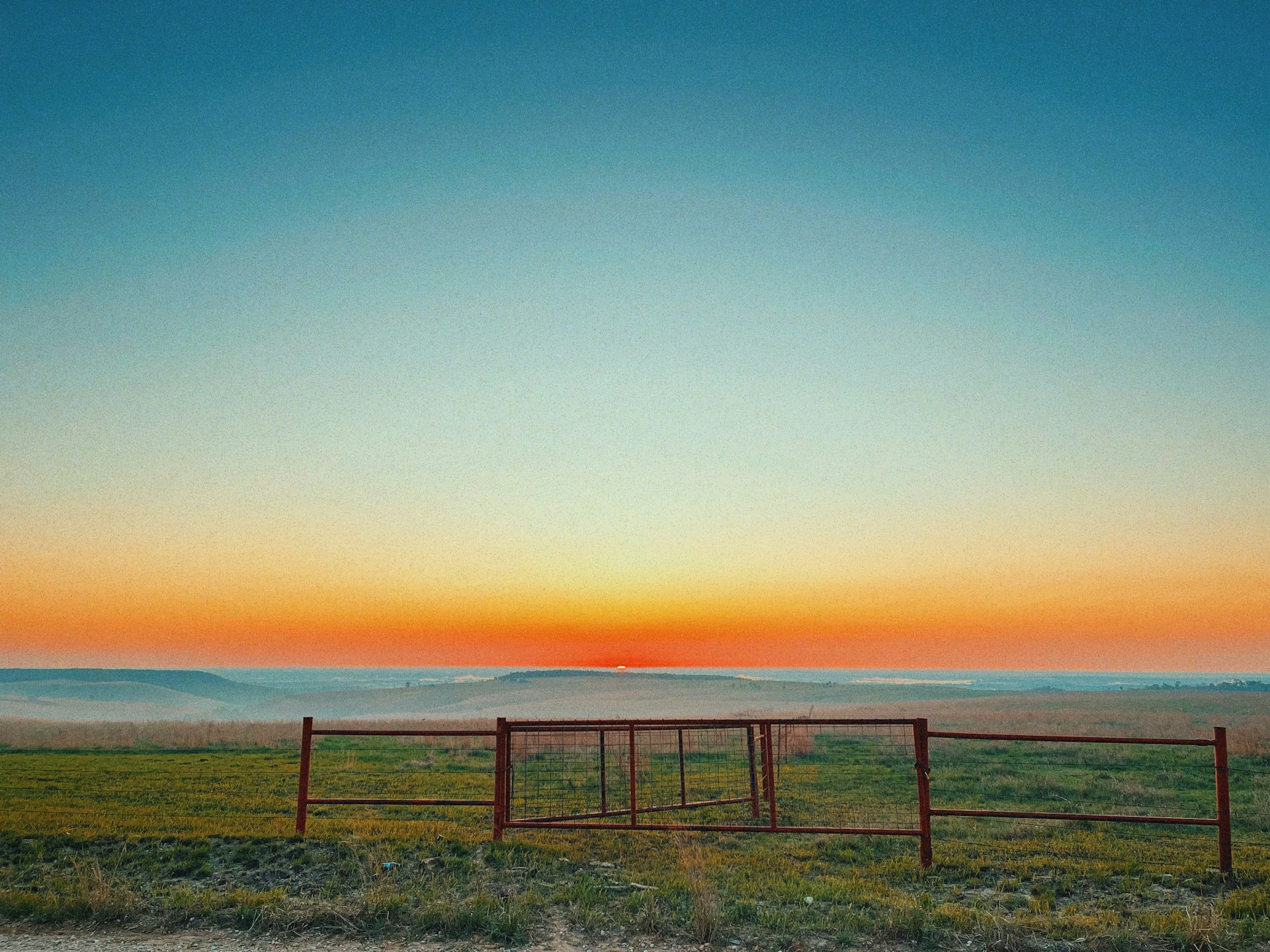 a red gate in a grassy field with a sunset in the background