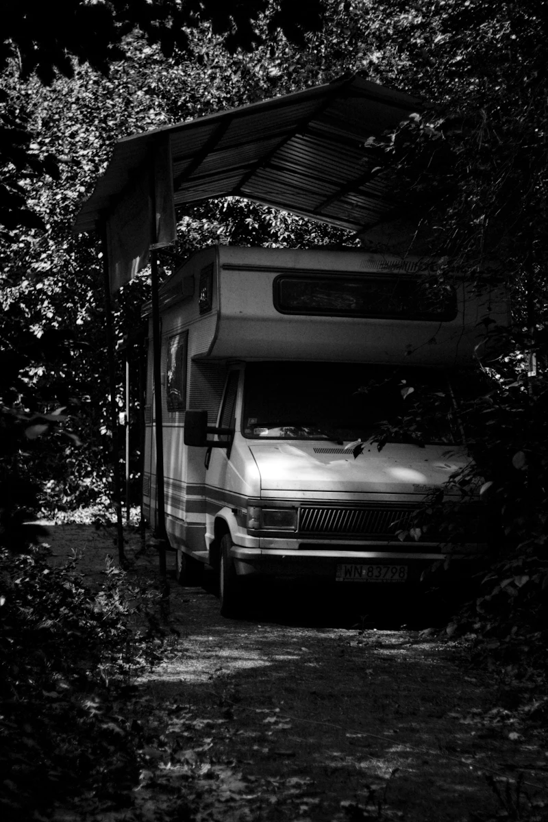 Van parked under a fabric canopy in a wooded campsite