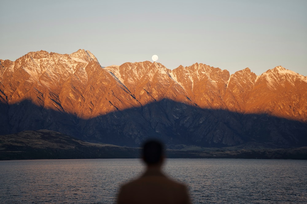 Ein Mann, der vor einem Gewässer mit Bergen im Hintergrund steht
