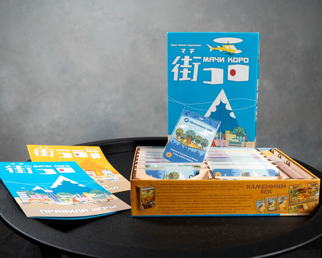 a black table topped with a box of books, A top-down view of randomly selected cards and components from Machi Koro and 