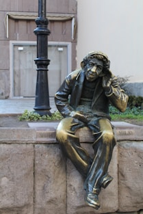 a bronze statue of a man sitting on a ledge