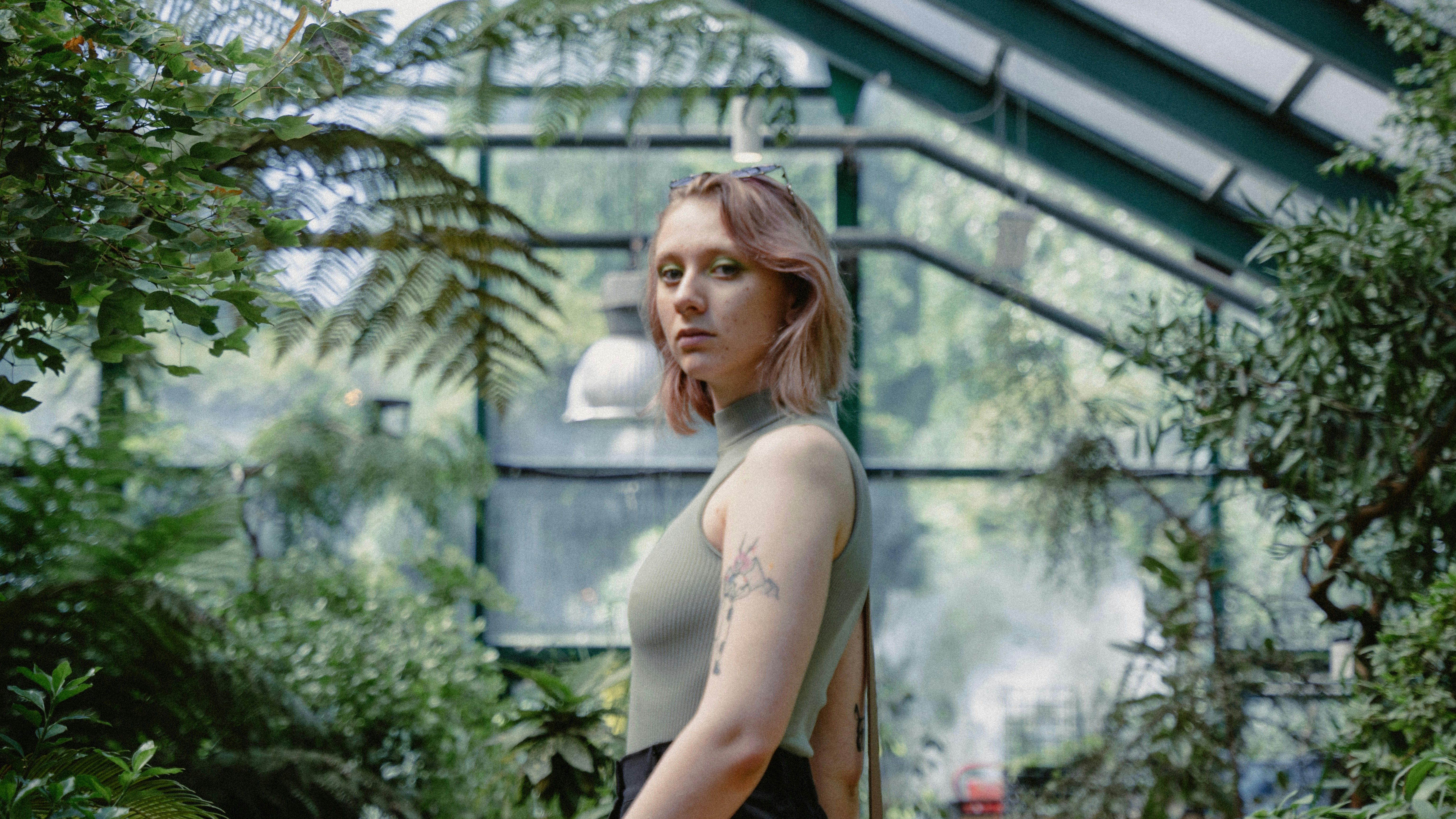 a woman standing in a greenhouse looking at the camera