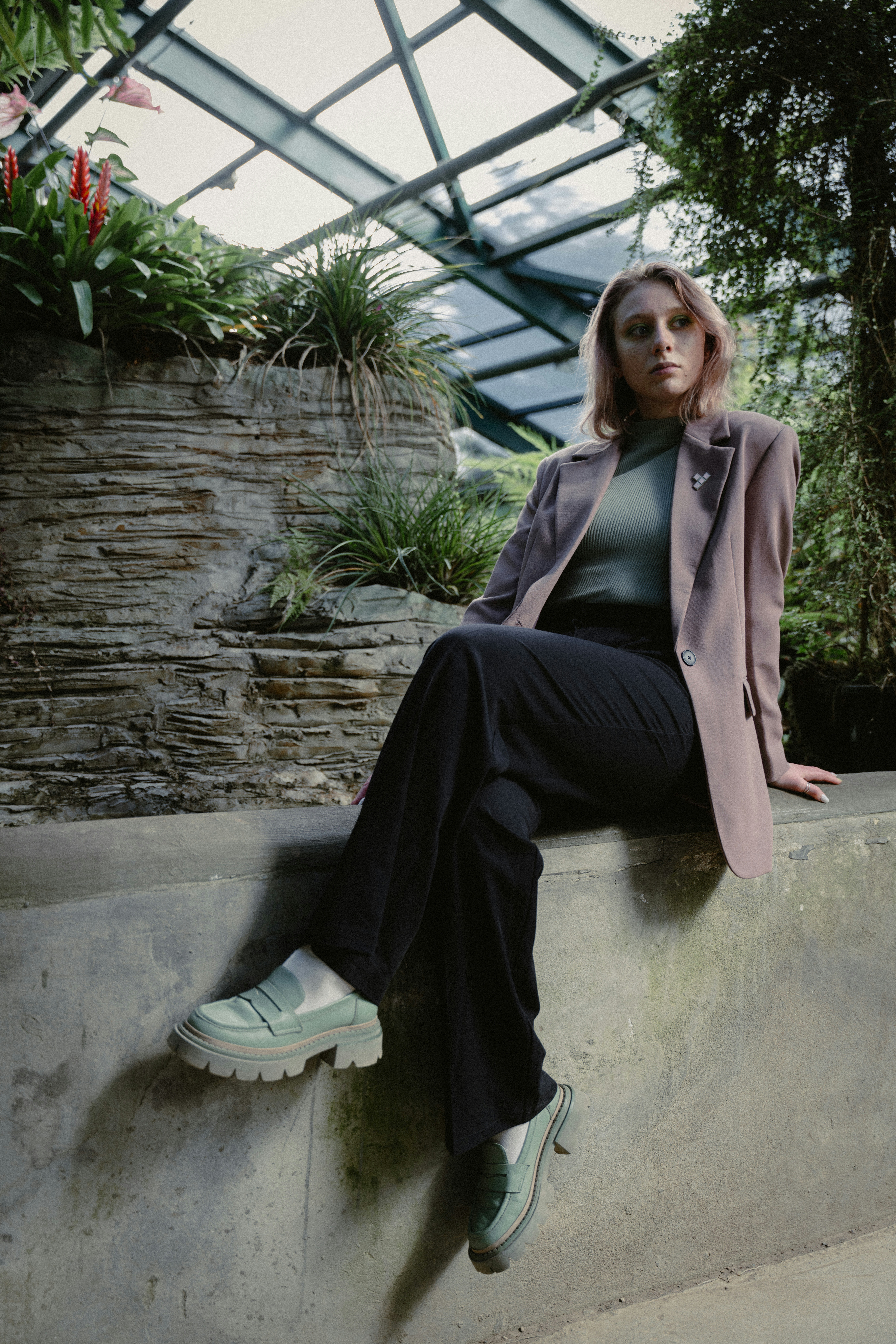 a woman sitting on a ledge in a greenhouse