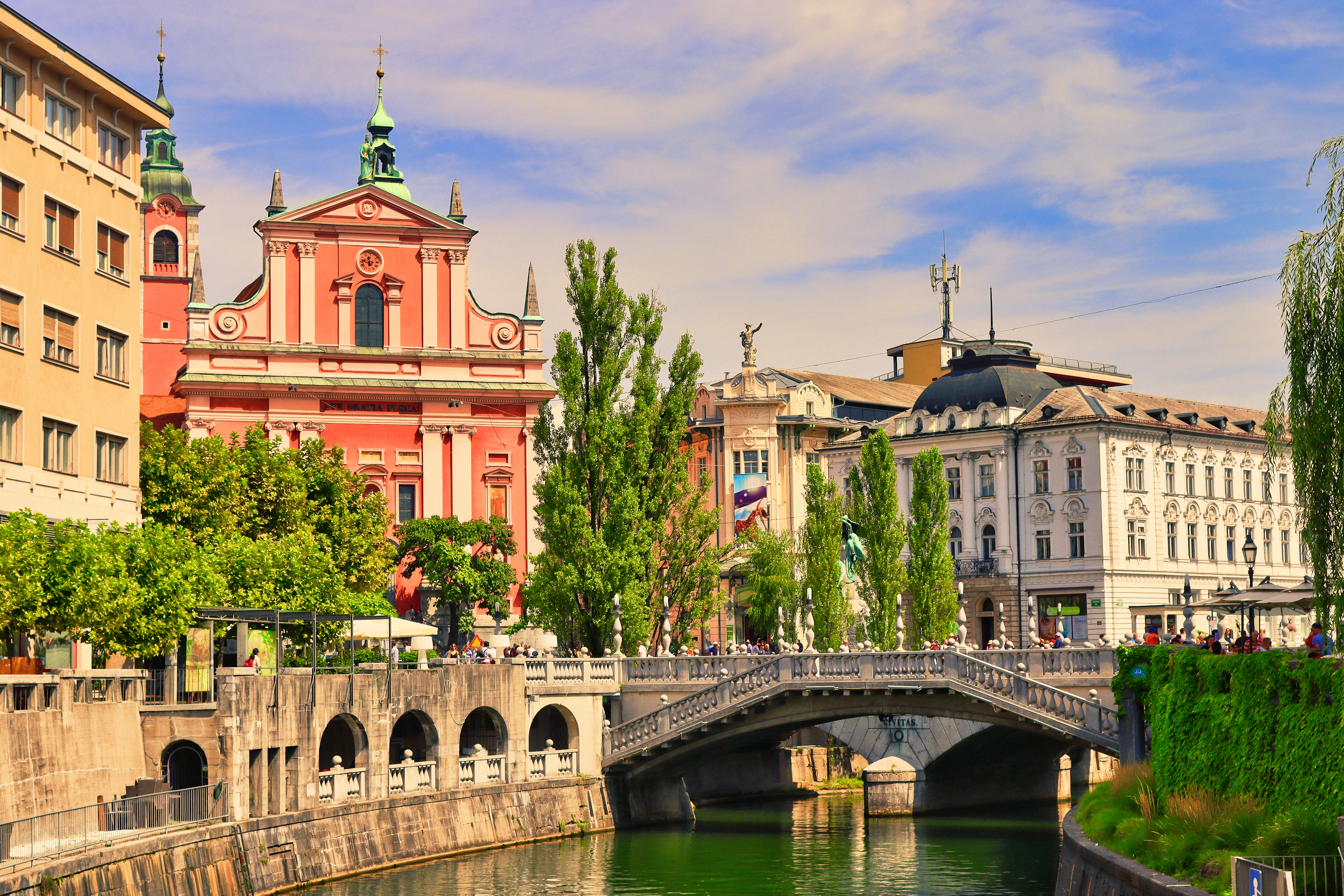 The pink Franciscan Church of the Annunciation and the stone arches of the Triple Bridge over the green Ljubljanica river in central Ljubljana