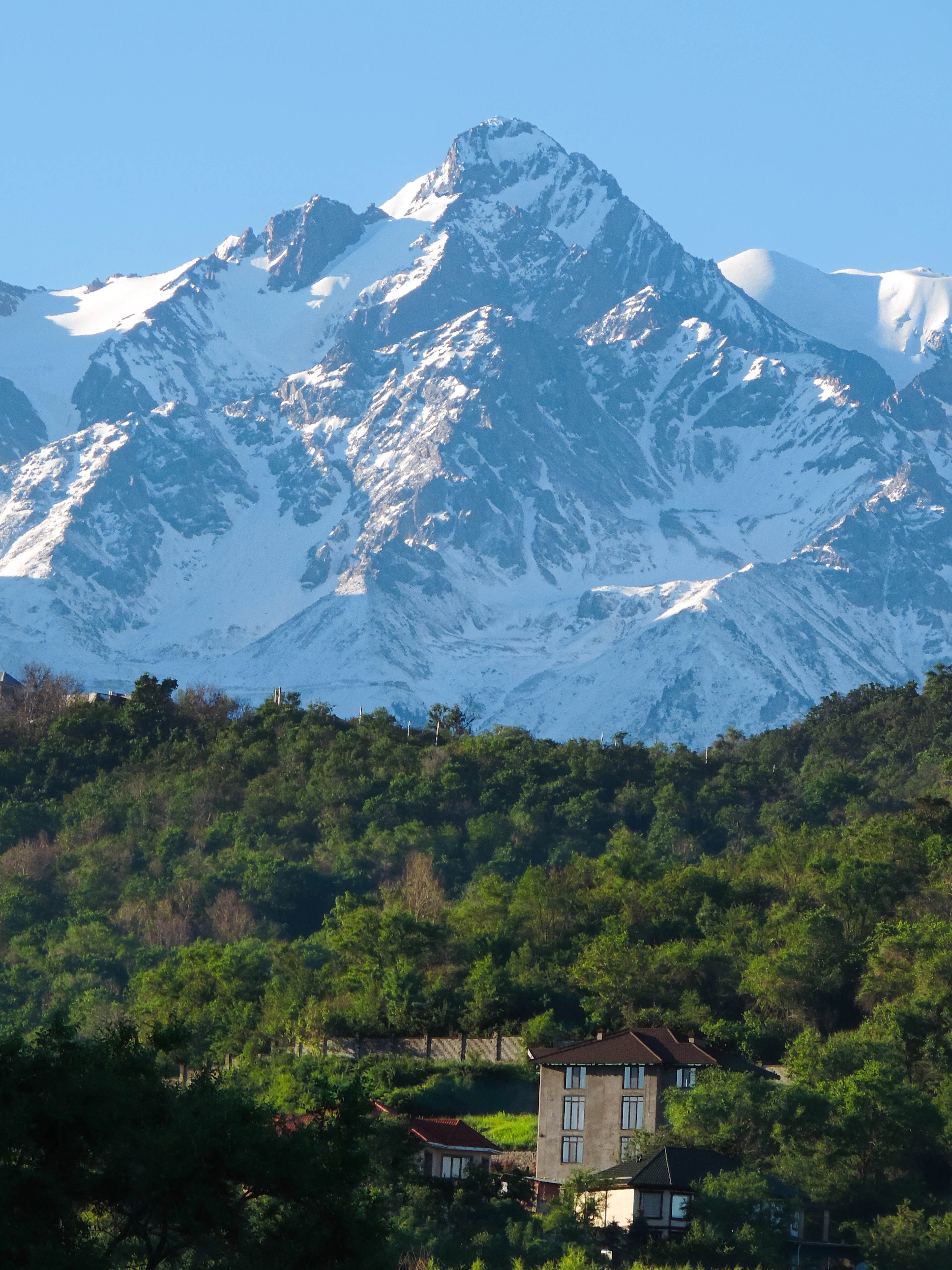 Snow-capped Tian Shan peak rising above green foothills and a house near Almaty.