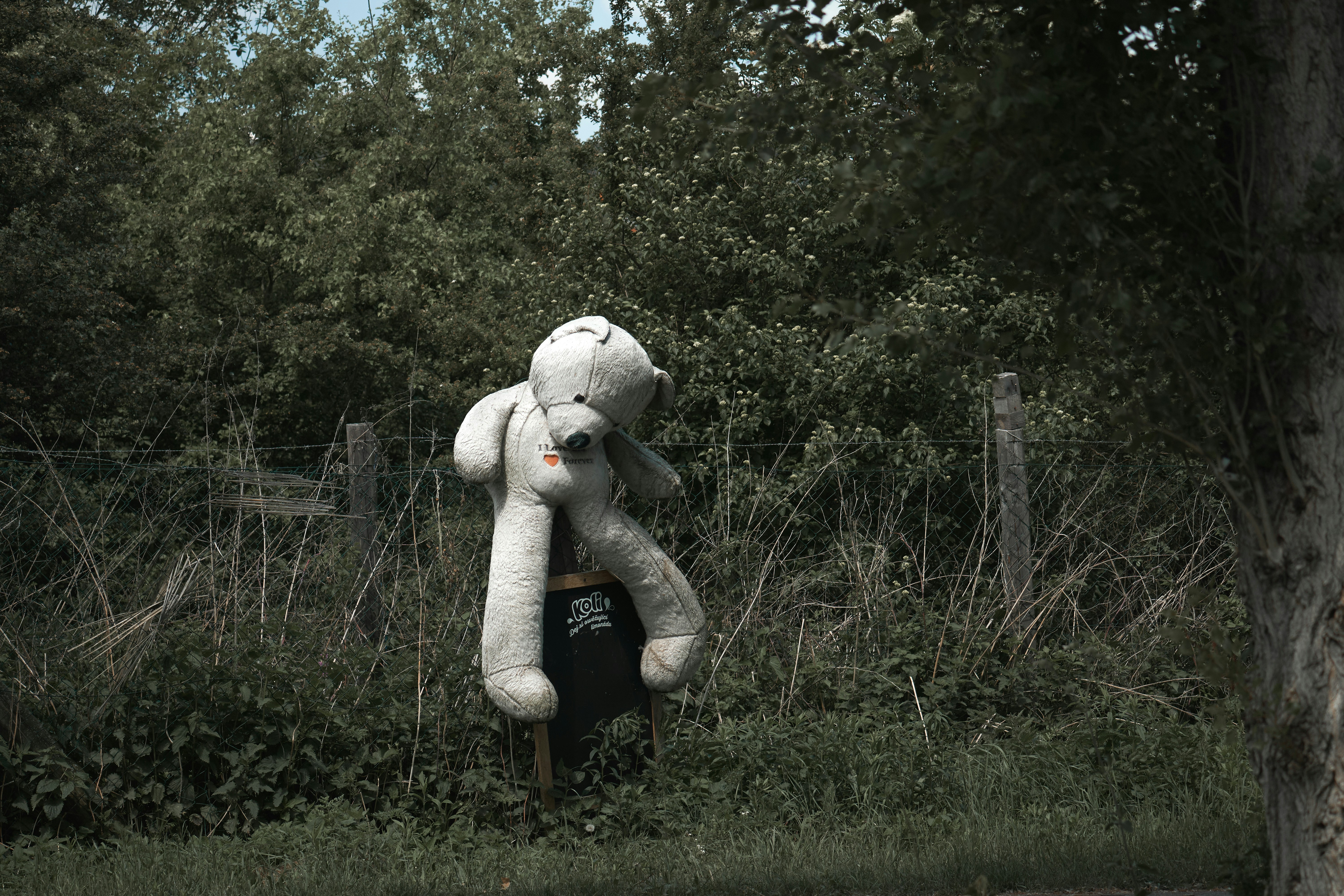 a large white teddy bear sitting on top of a trash can