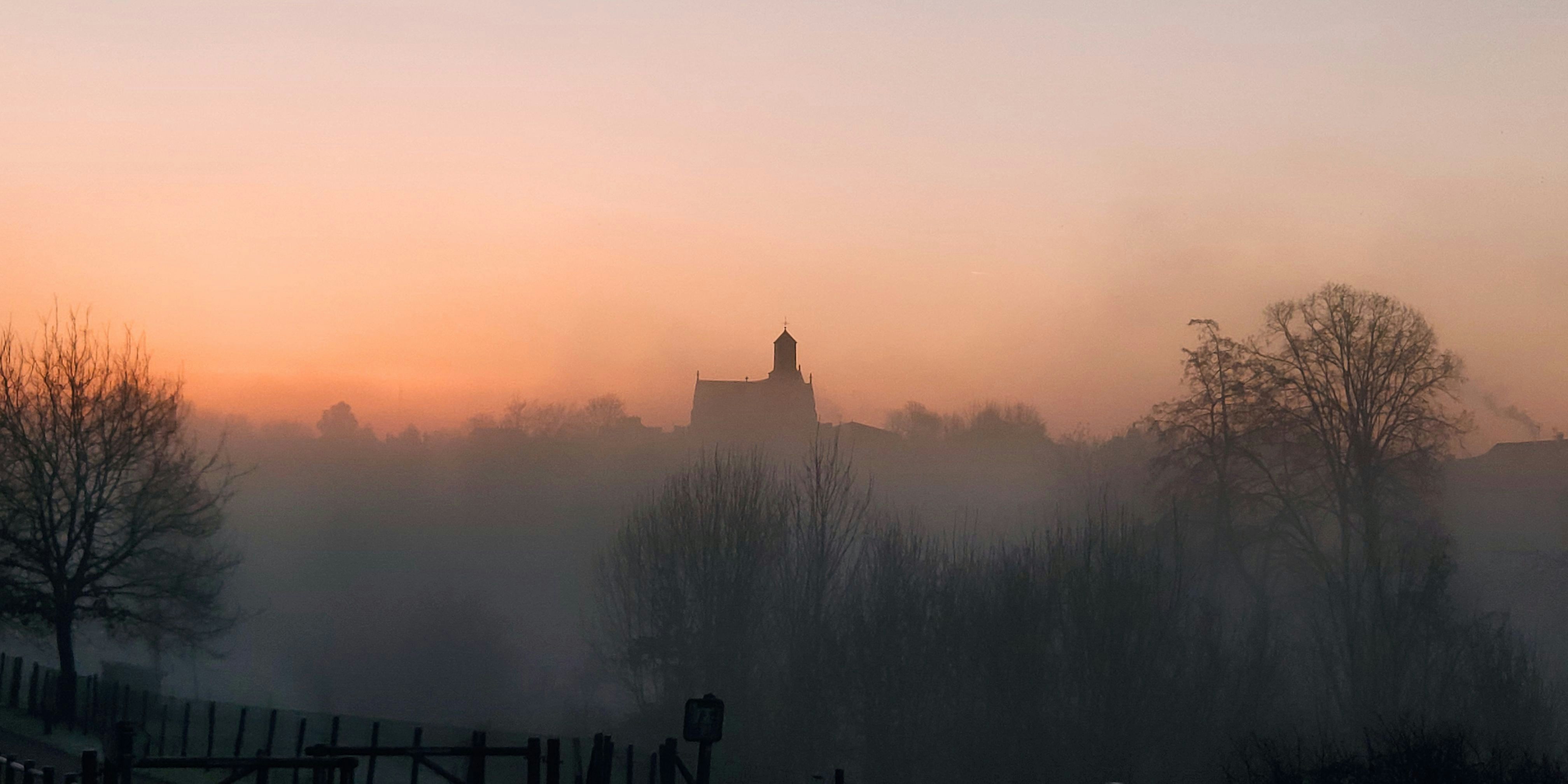 a foggy sunrise with a church in the distance