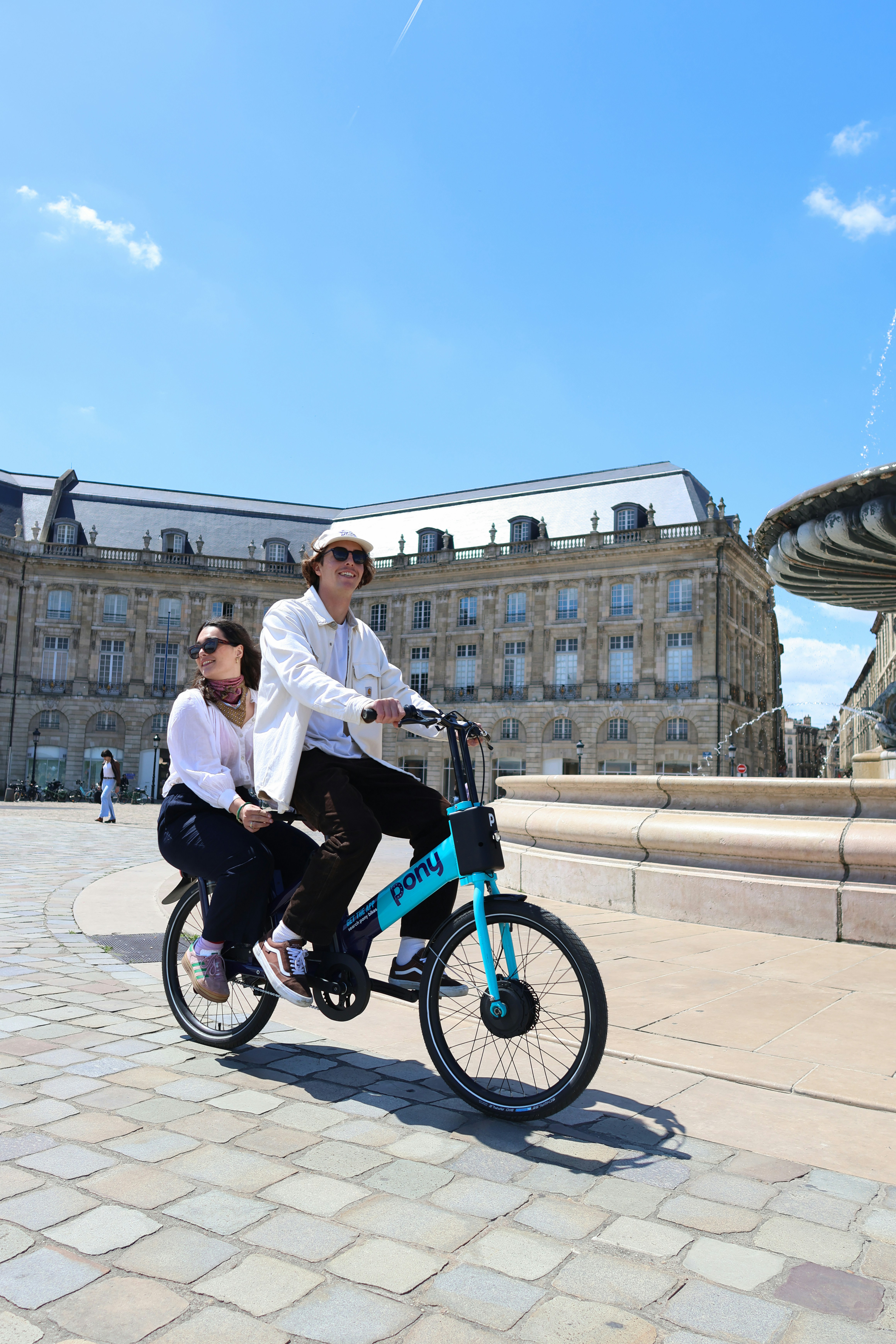 a man and a woman riding a bike in front of a fountain